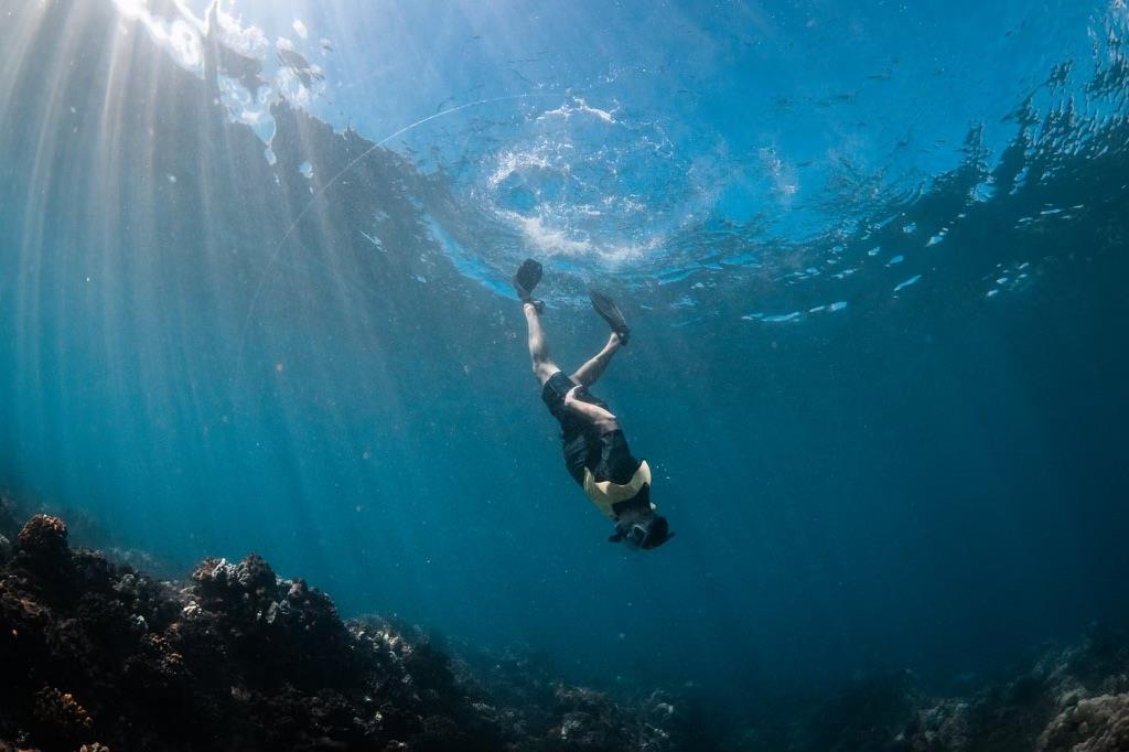 Swimmer explores underwater world among coral formations in bright sunlight.