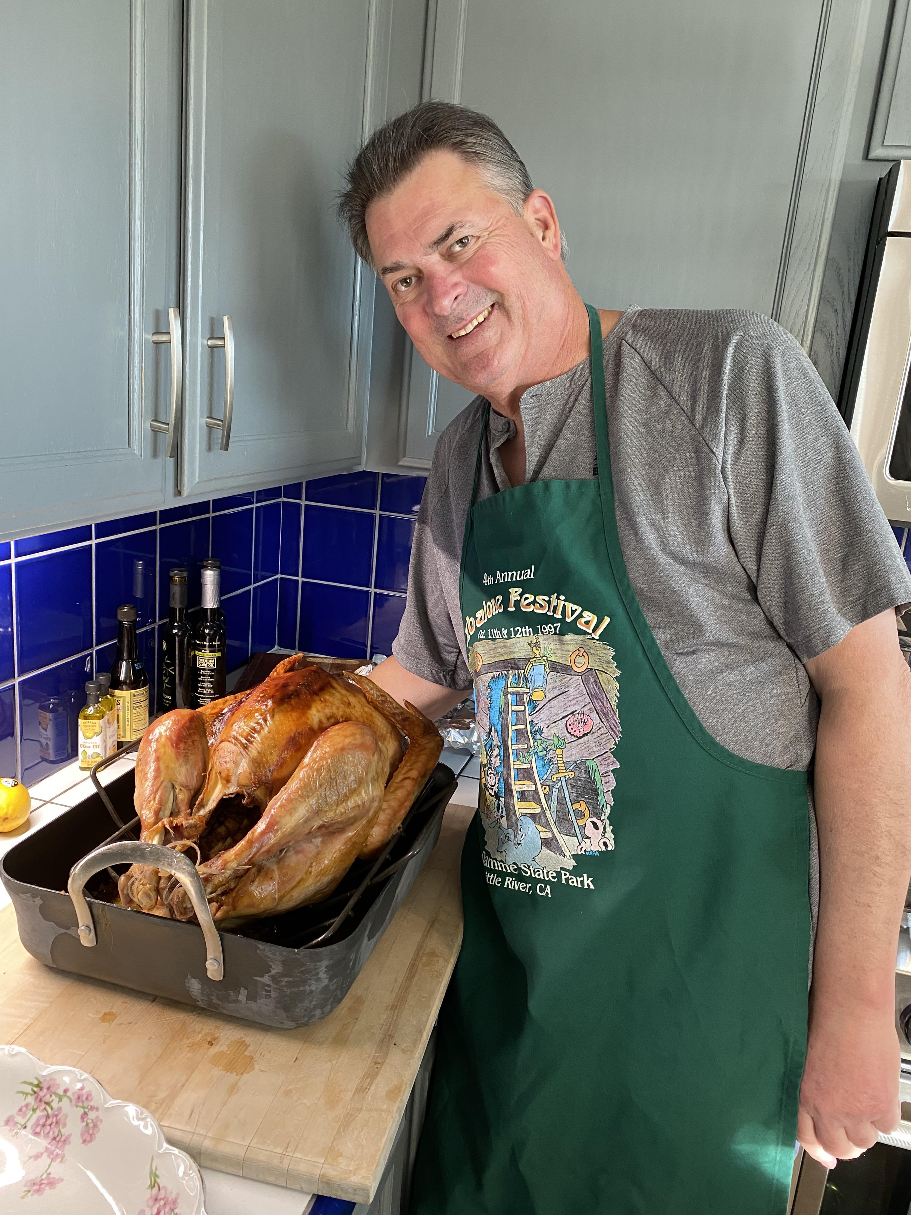 A man stands next to a perfectly roasted turkey, ready for a family gathering in the kitchen.