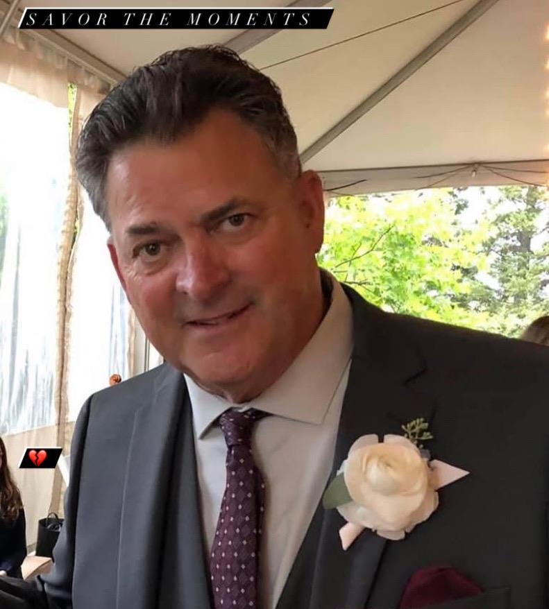 Man dressed in formal wear smiles at a lively gathering in a beautifully decorated space.