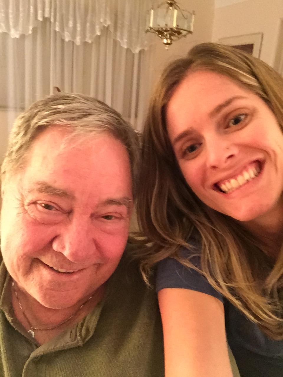 Two family members are smiling widely while posing close together in a warm, inviting living room.