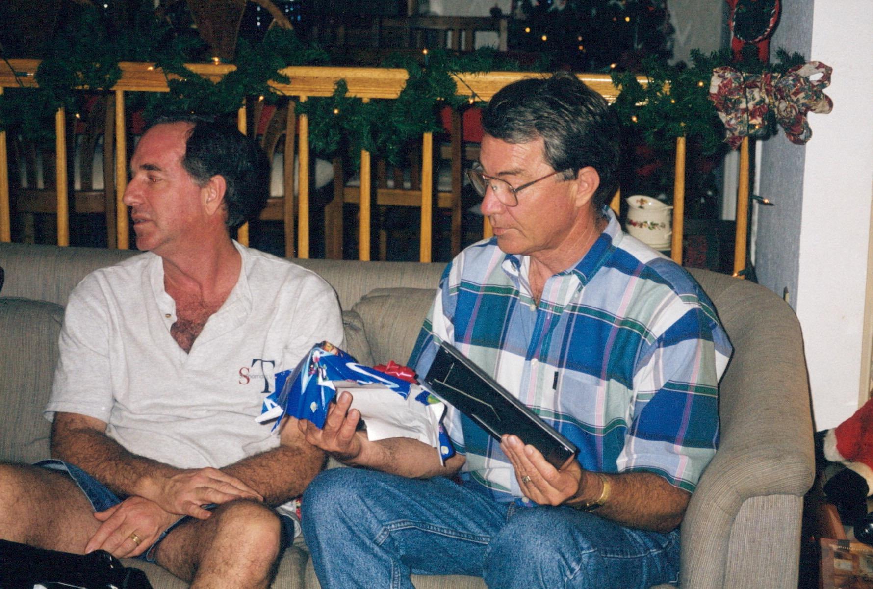 Friends laugh and enjoy unwrapping gifts on a cozy couch amid decorations.