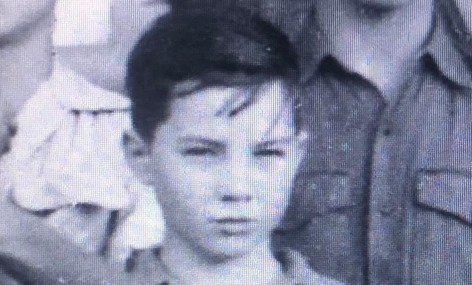 A serious young boy with short hair is surrounded by friends in a black-and-white photo.