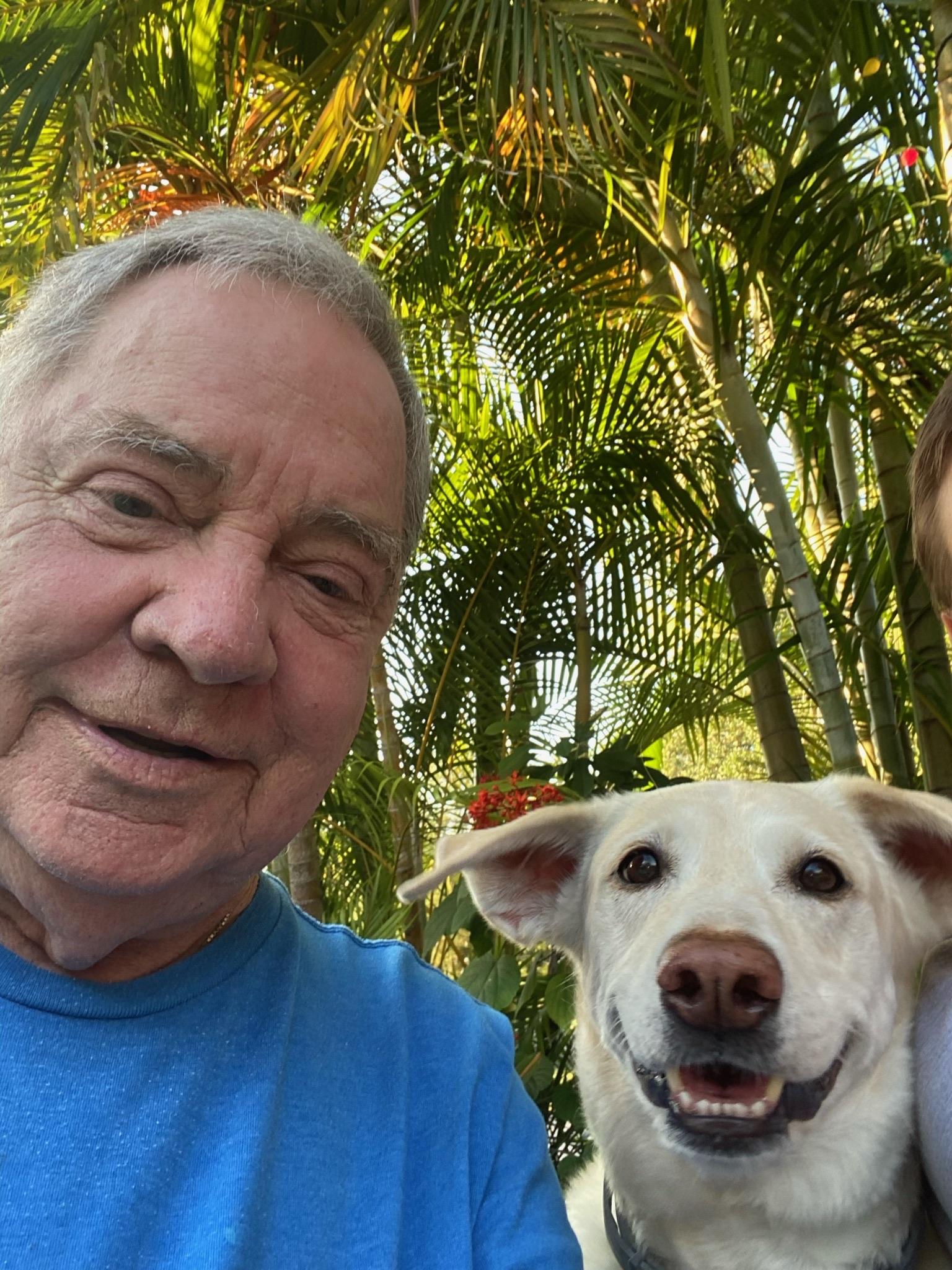A man and a smiling dog share a joyful moment in a vibrant garden filled with greenery.