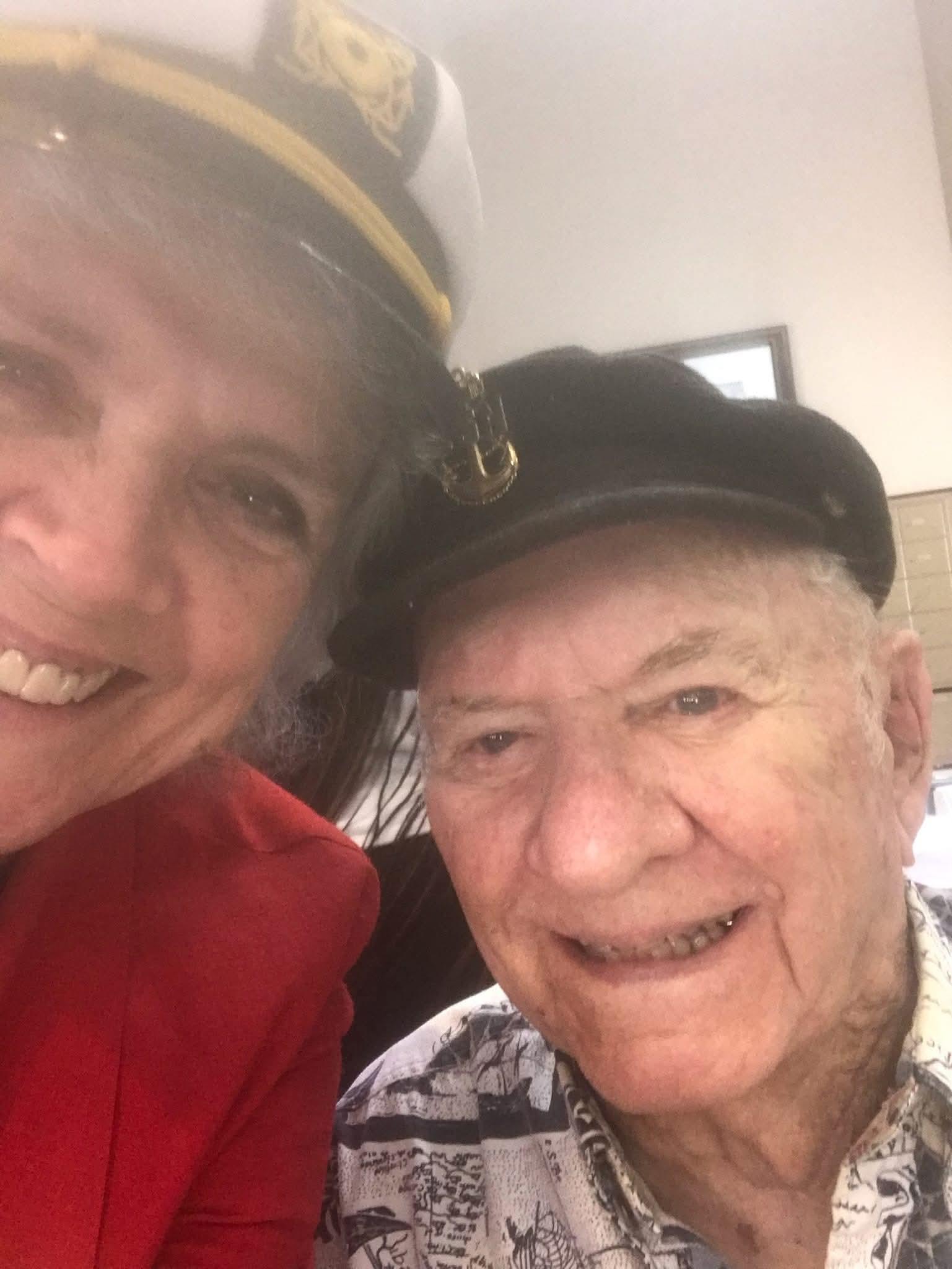 Elderly man and woman wearing hats smile for a close-up photo during a community event.