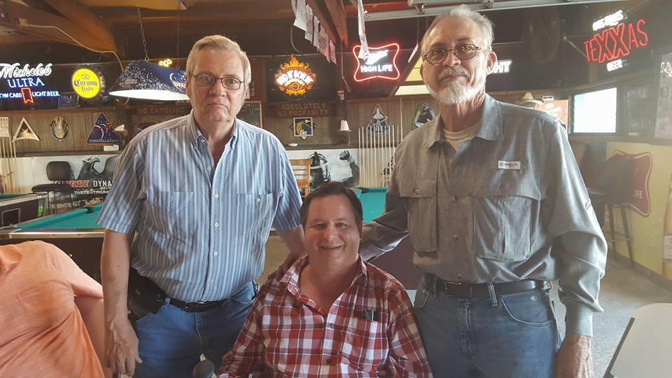 Three friends pose together in a relaxed bar setting, enjoying their time and conversation.