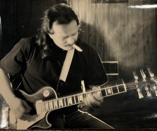 Musician immersed in playing guitar with a cigarette in hand, creating a nostalgic atmosphere.