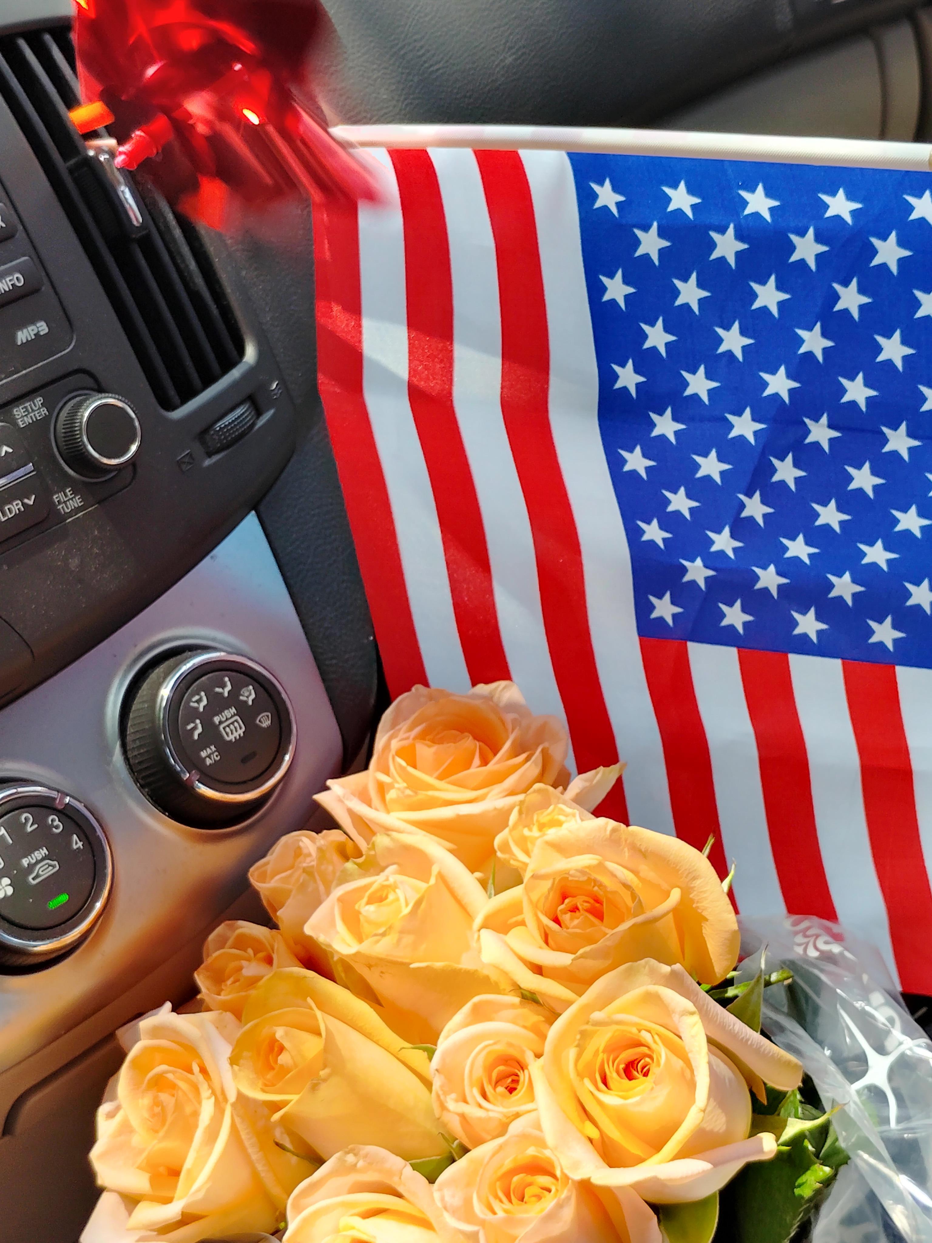 Yellow roses in a car next to an American flag display pride in a summer celebration.