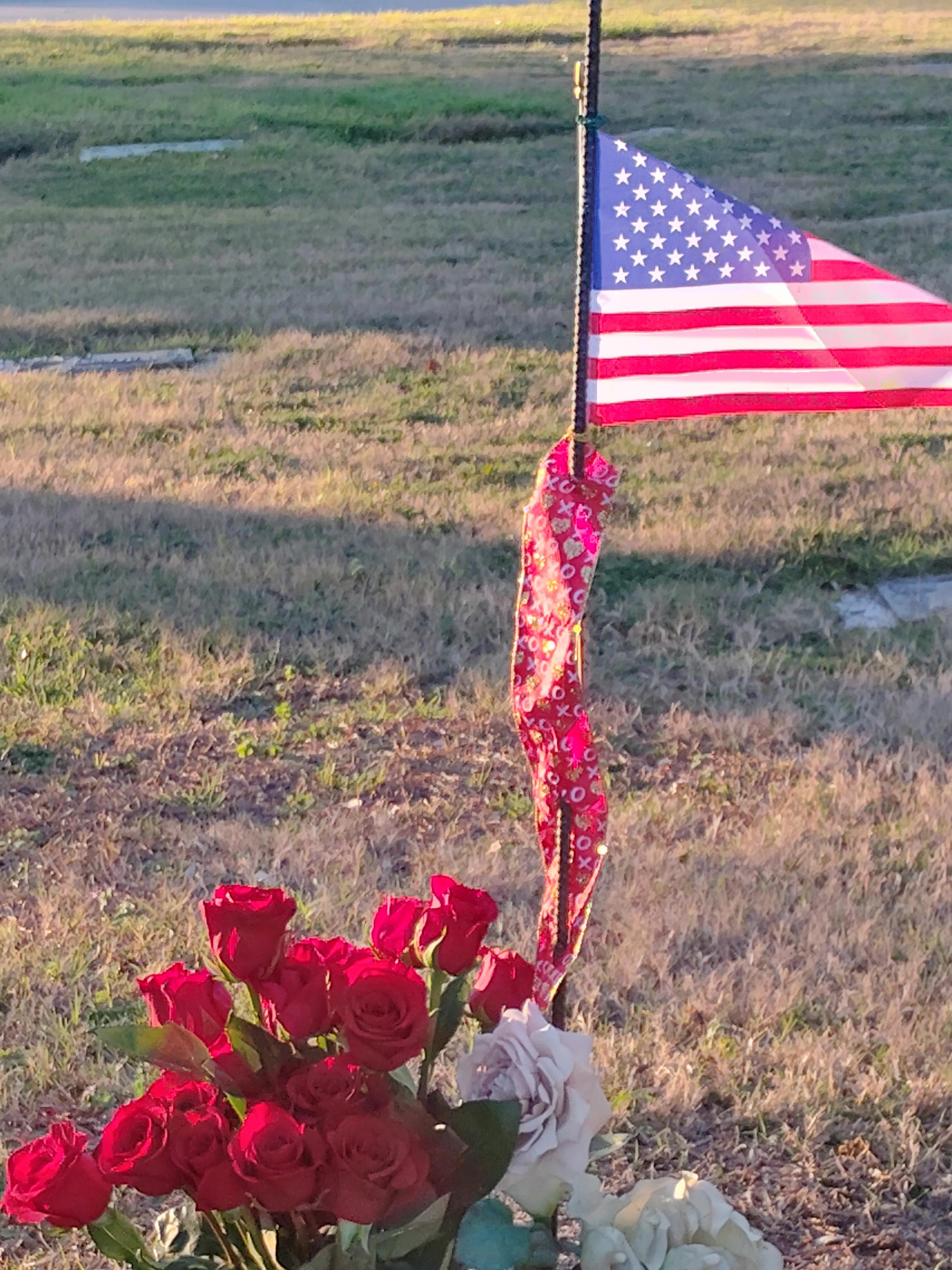 Roses are arranged near a flag on grass during evening hours in a quiet location.