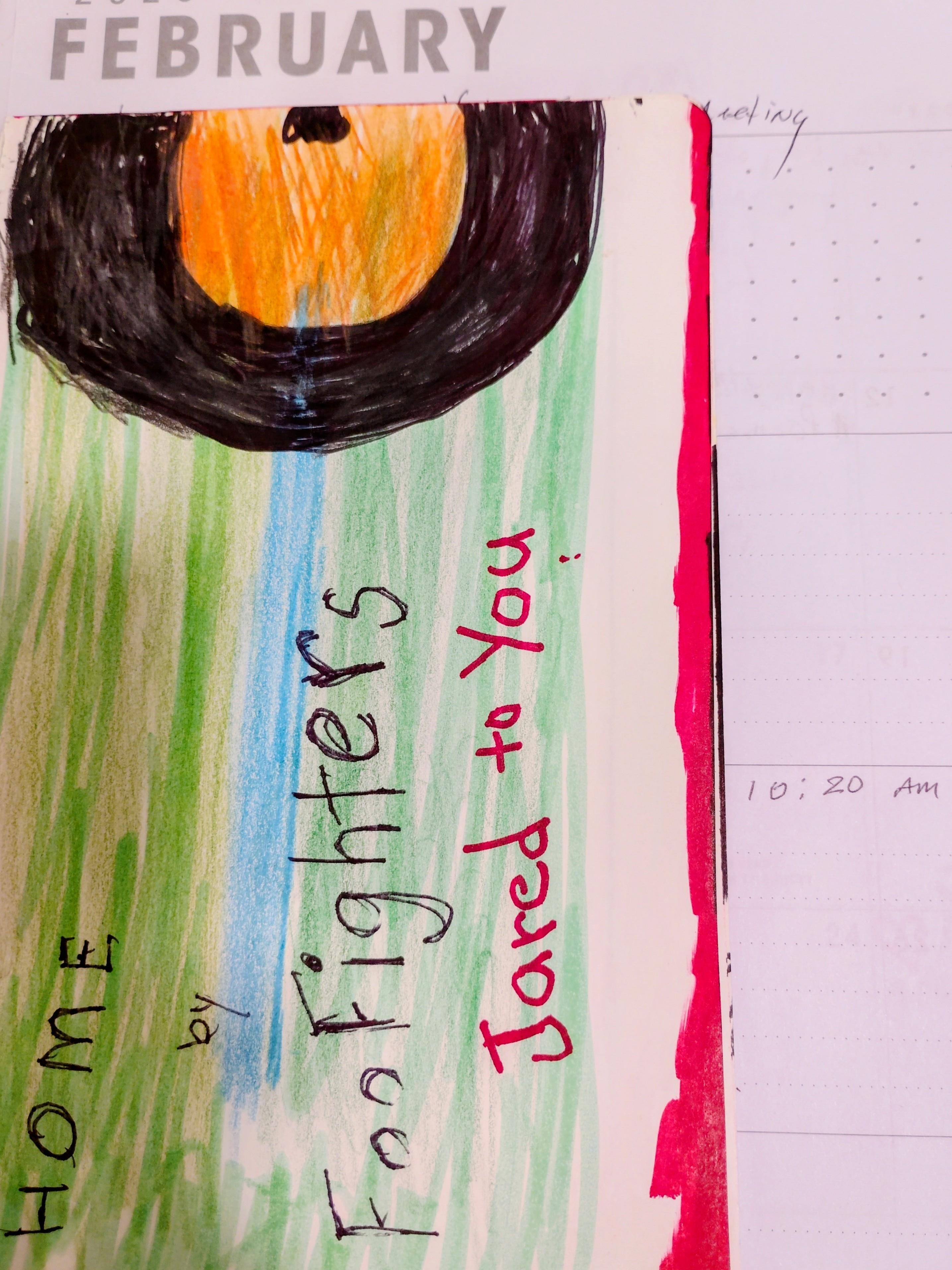 A child created a drawing with a sun and text about Foo Fighters on a notebook page.