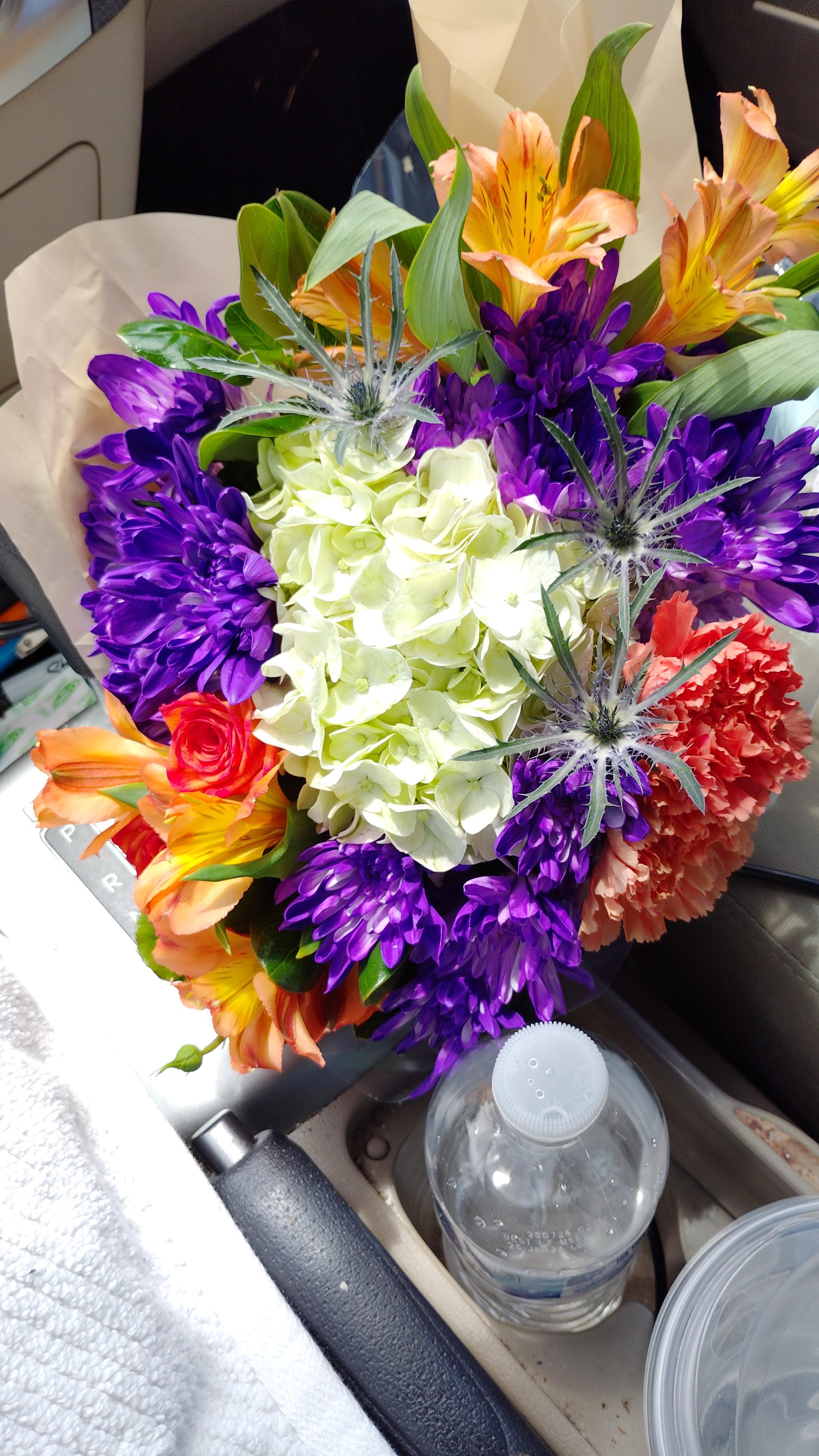 A vibrant bouquet of hydrangeas, roses, and asters is arranged on a table.