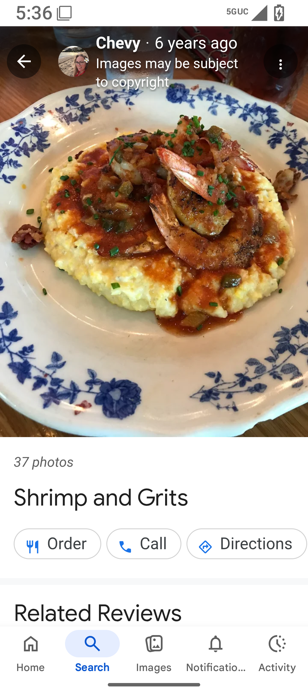 Dish features shrimp and grits with sauce, served with herbs on a decorative plate.
