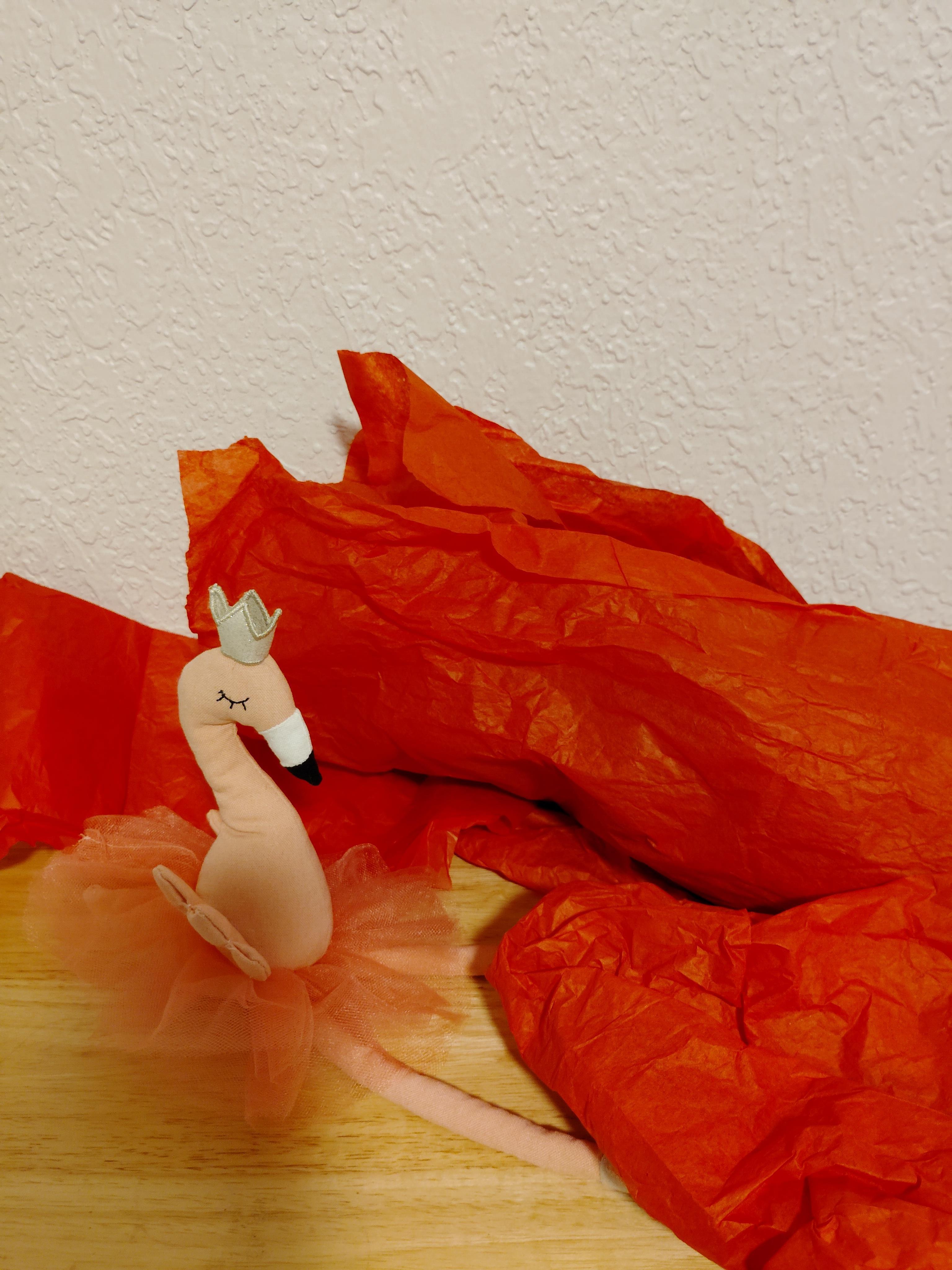 A small figure rests on a table next to crumpled red paper pieces. The scene shows a playful setup.