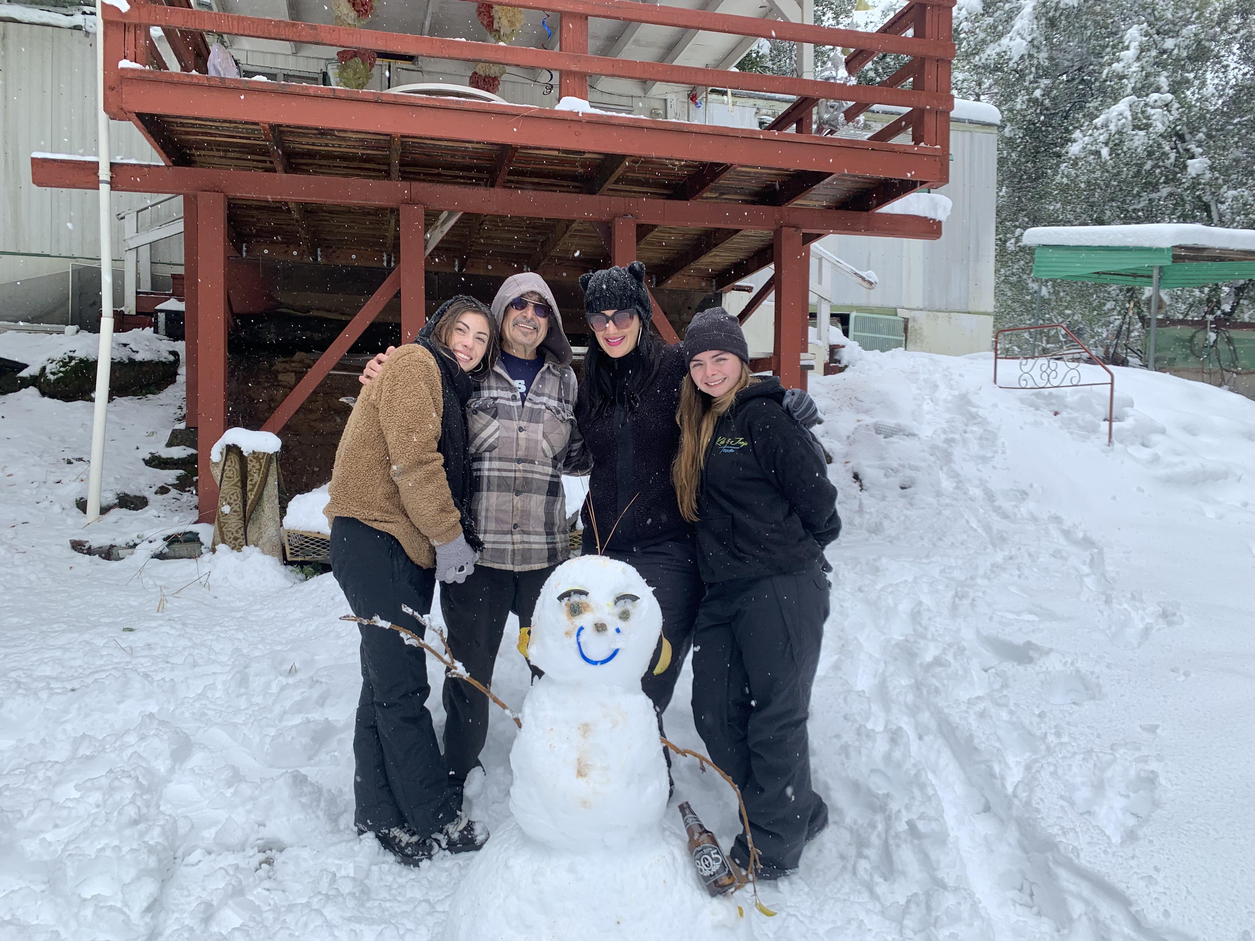 Four friends enjoy a fun day outside, crafting a snowman in front of a cabin covered in snow.