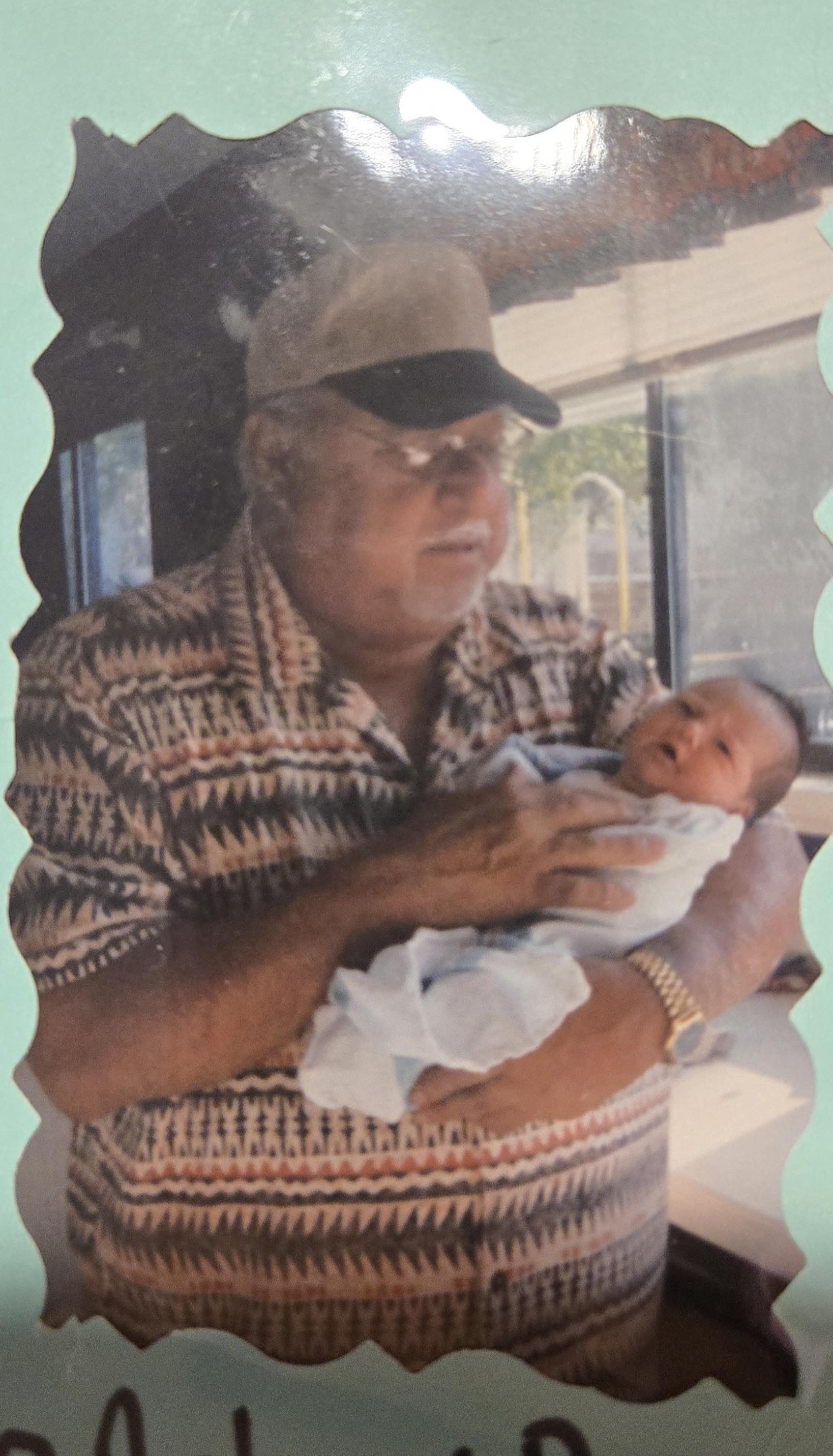 A grandfather gently holds a newborn baby while seated, displaying a tender family moment.