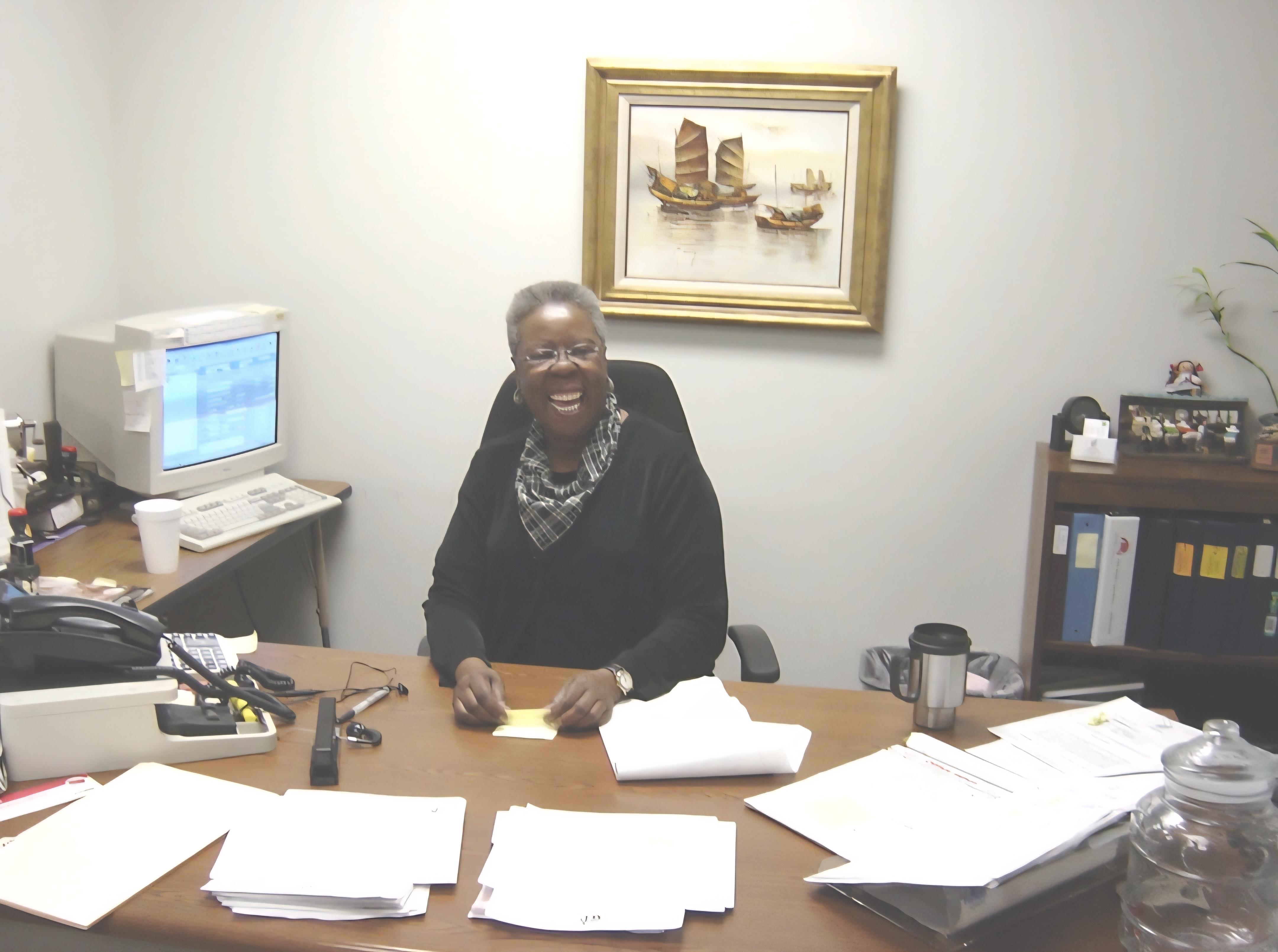 A happy woman works at her desk, surrounded by papers in a daytime office.