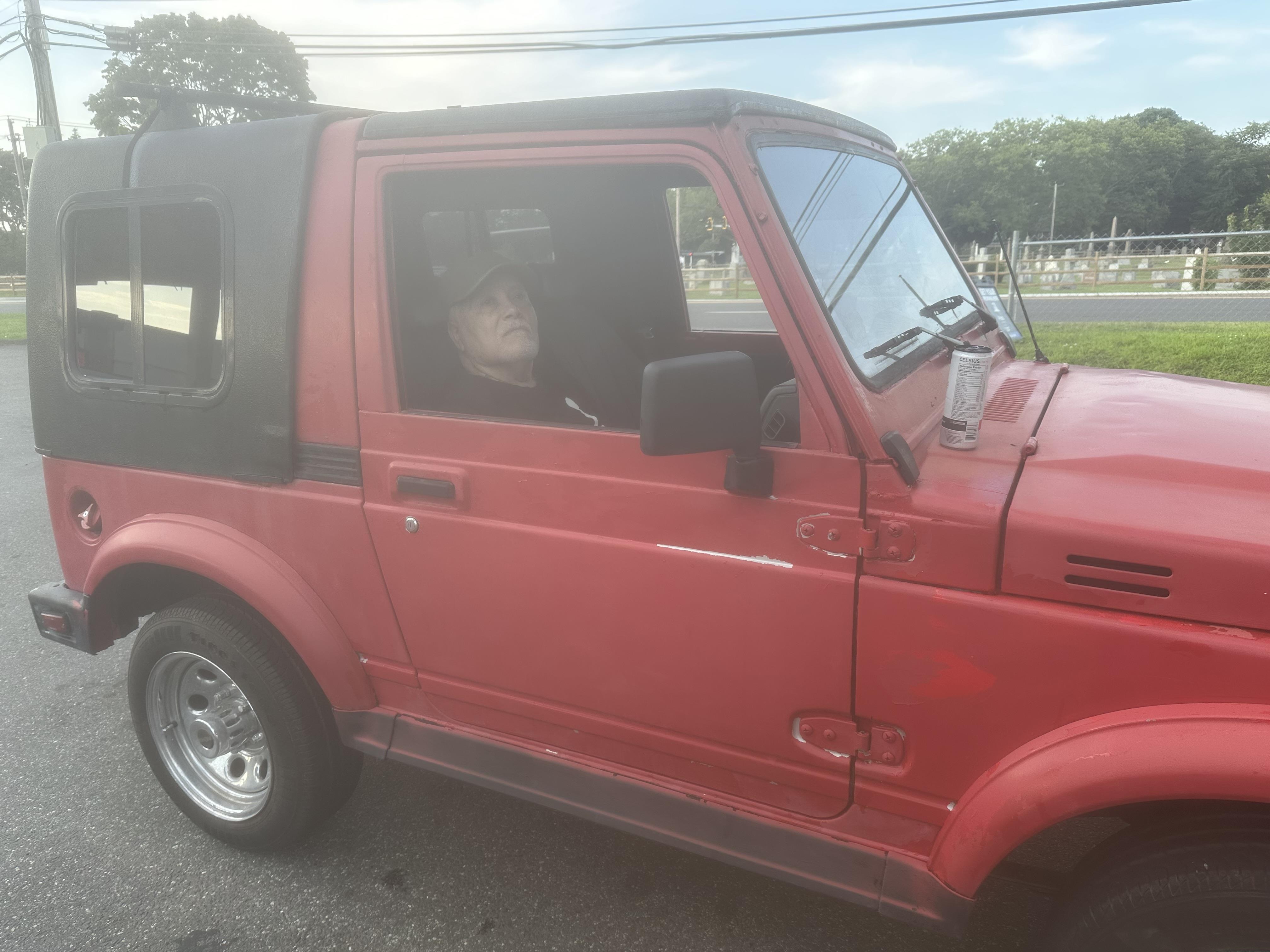 Someone is driving a bright red off-road vehicle with a soft top, enjoying the sunny weather.