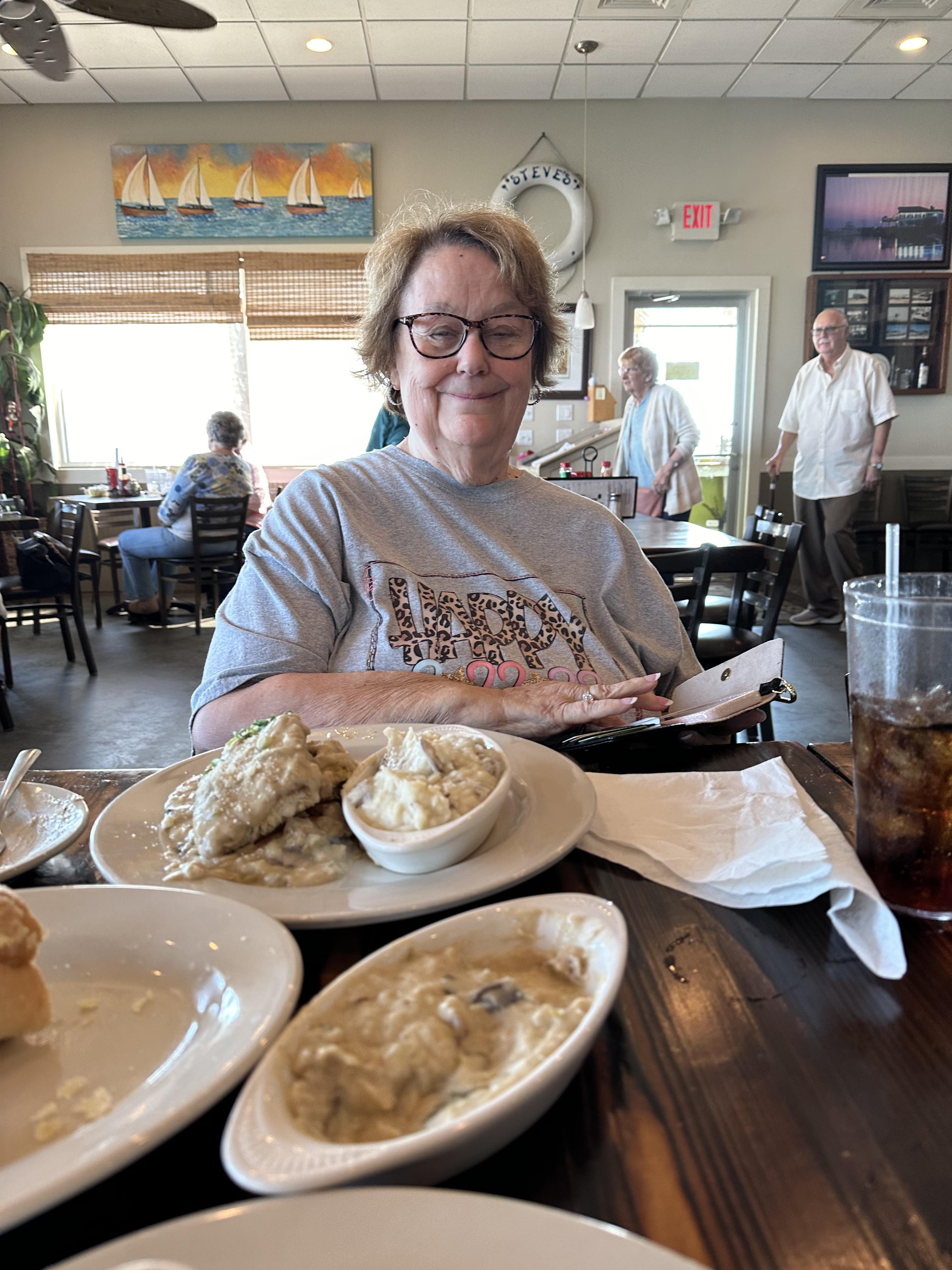 A woman sits at a table filled with delicious food, enjoying her lunch with friends nearby.