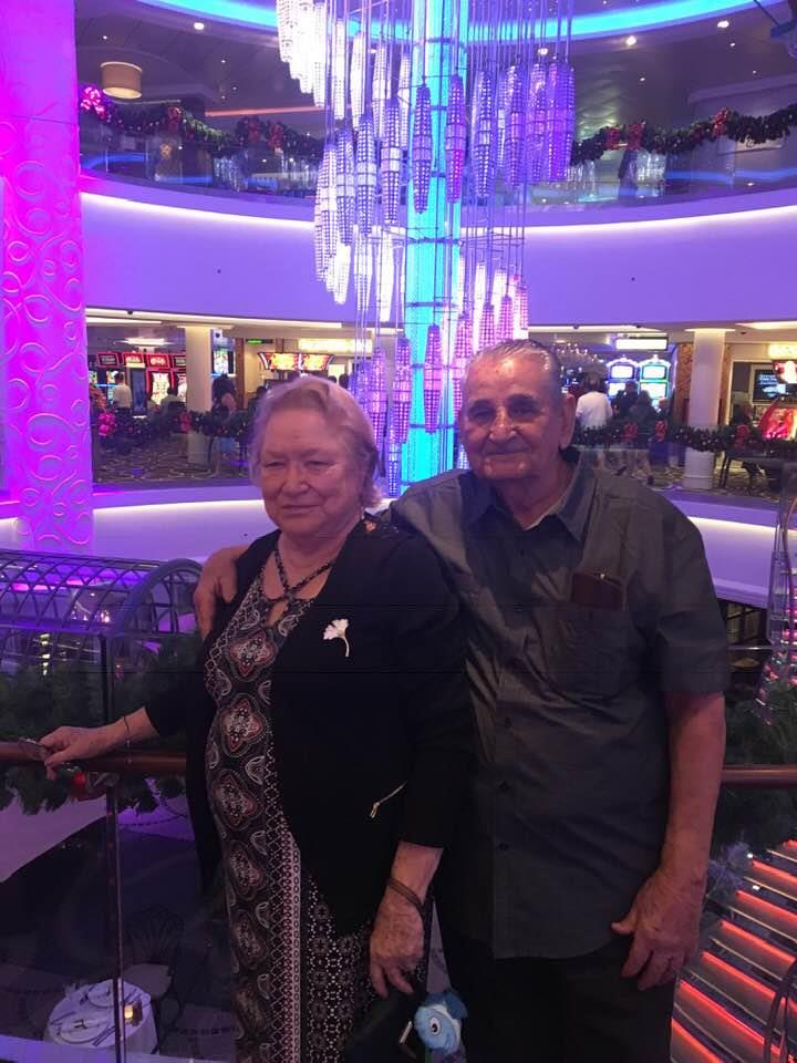 A couple stands together, smiling, near a colorful chandelier in a bustling casino environment.