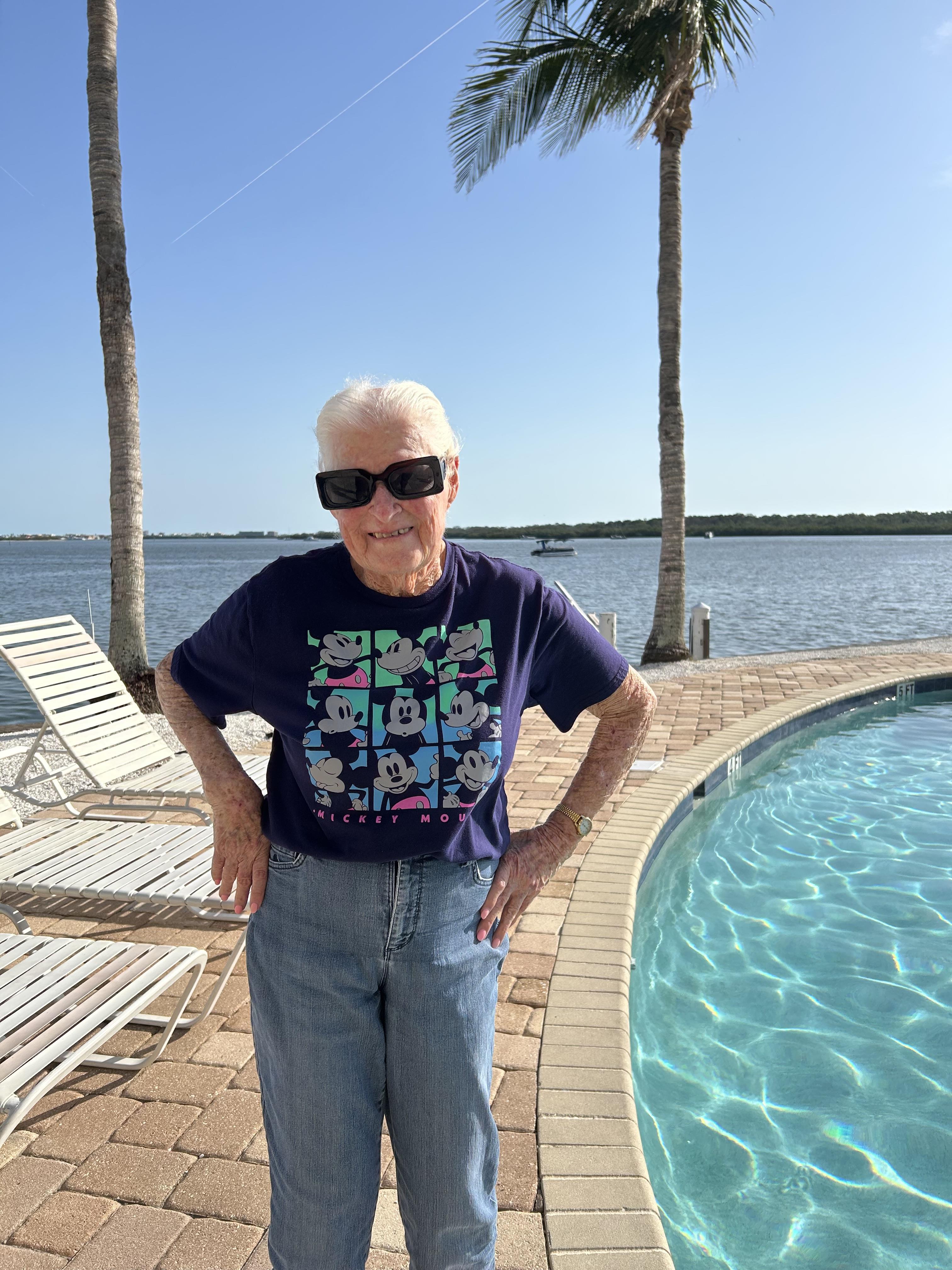 Older adult stands confidently by a pool on a warm, sunny day surrounded by palm trees.