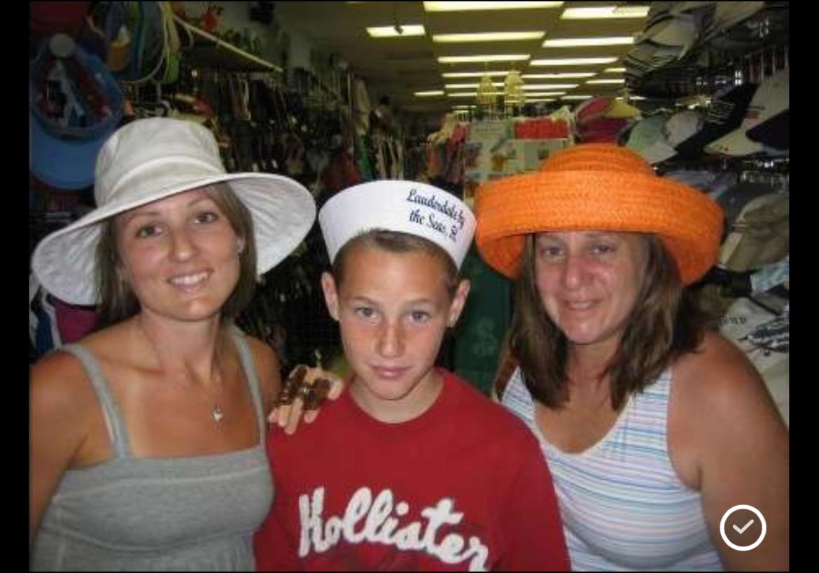 Three individuals are smiling and trying on different hats inside a well-stocked clothing store.