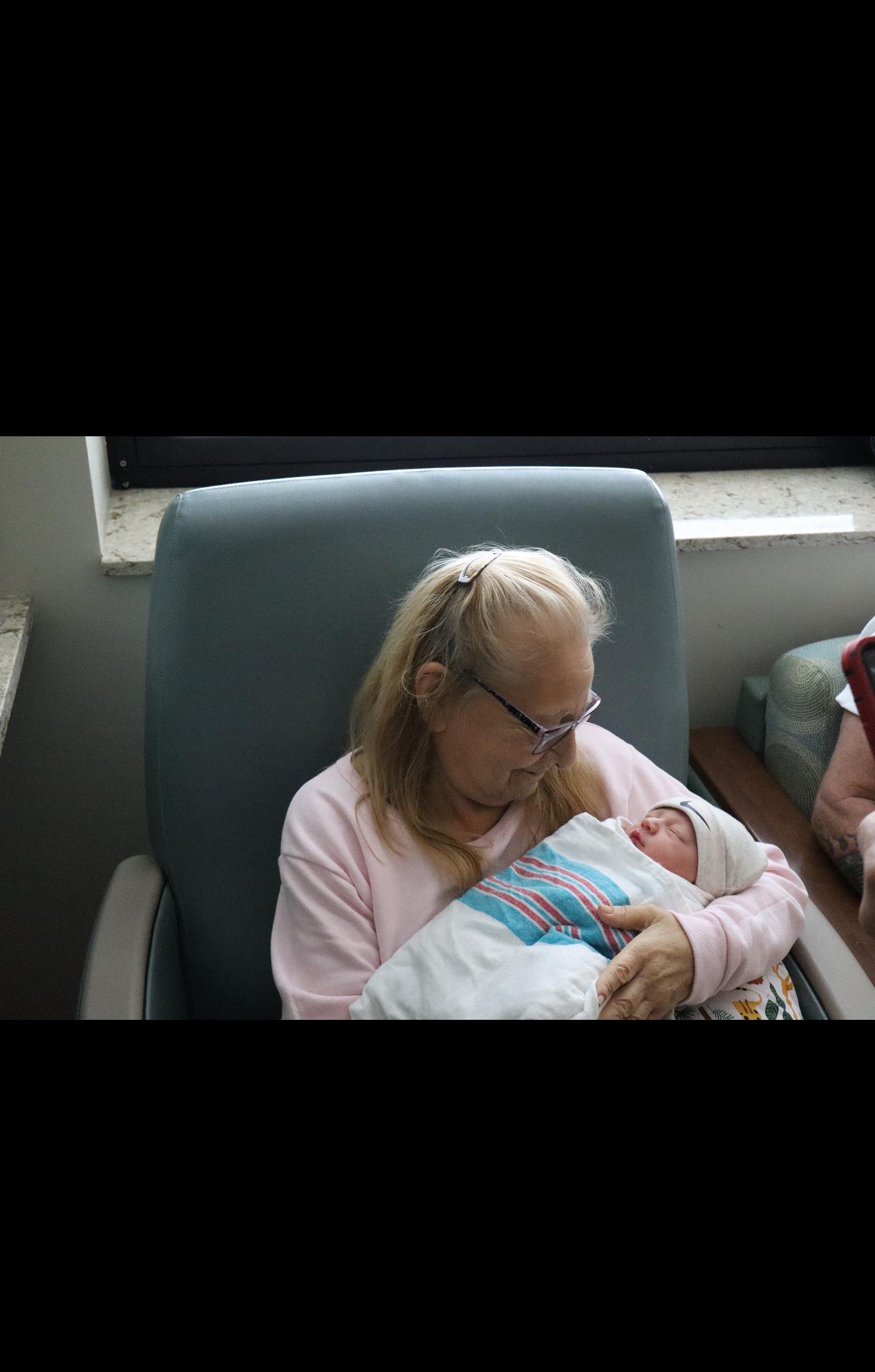 A loving grandmother cuddles her newborn grandchild in a hospital room, sharing a tender moment.