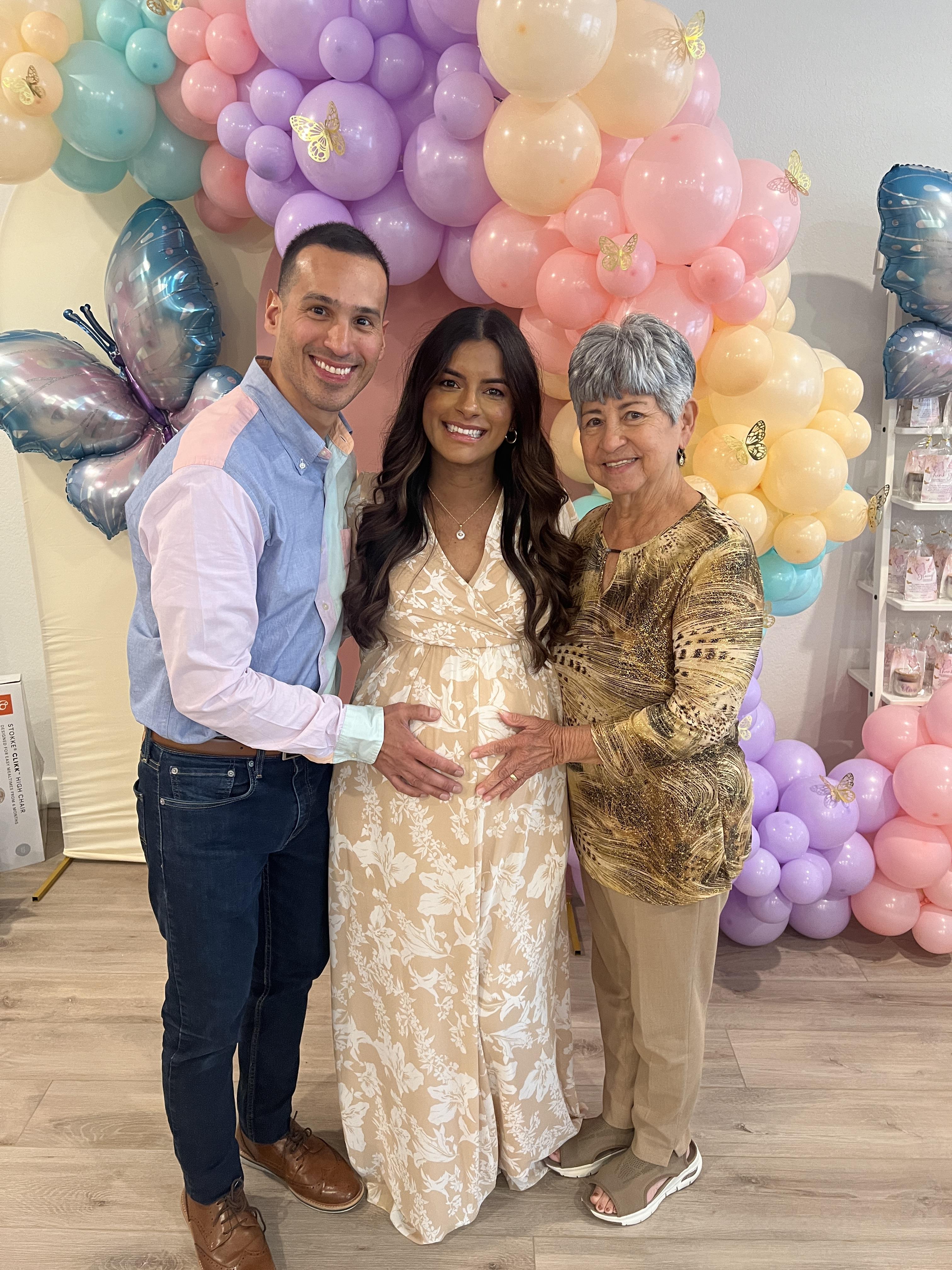 A couple and a grandmother gather to celebrate a baby shower with vibrant balloon decor.