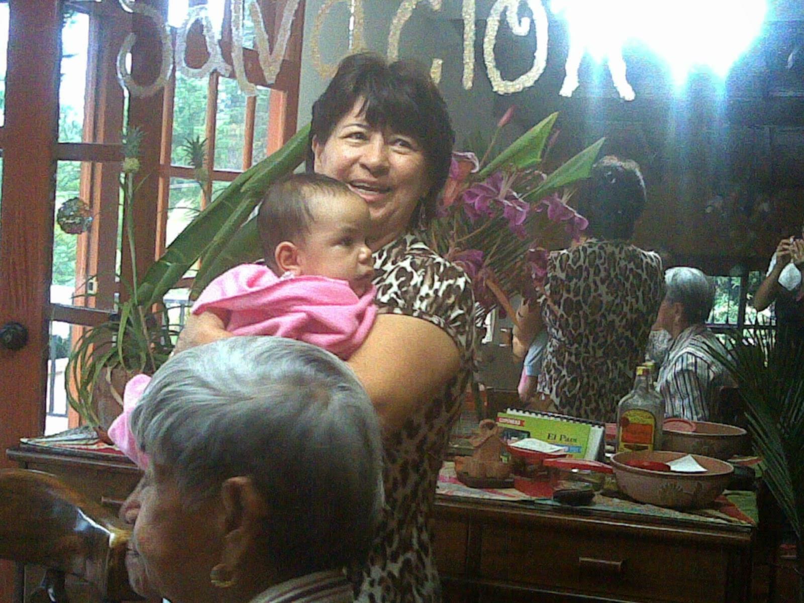 A cheerful woman embraces a baby, surrounded by loved ones in a warm, inviting atmosphere.
