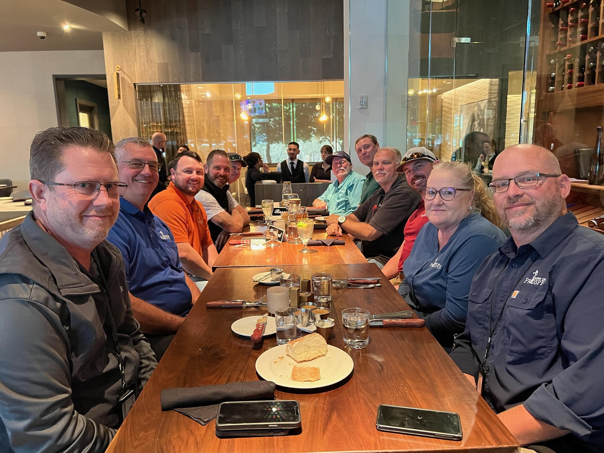 Friends gather around a long table, sharing food and laughter in a busy restaurant.