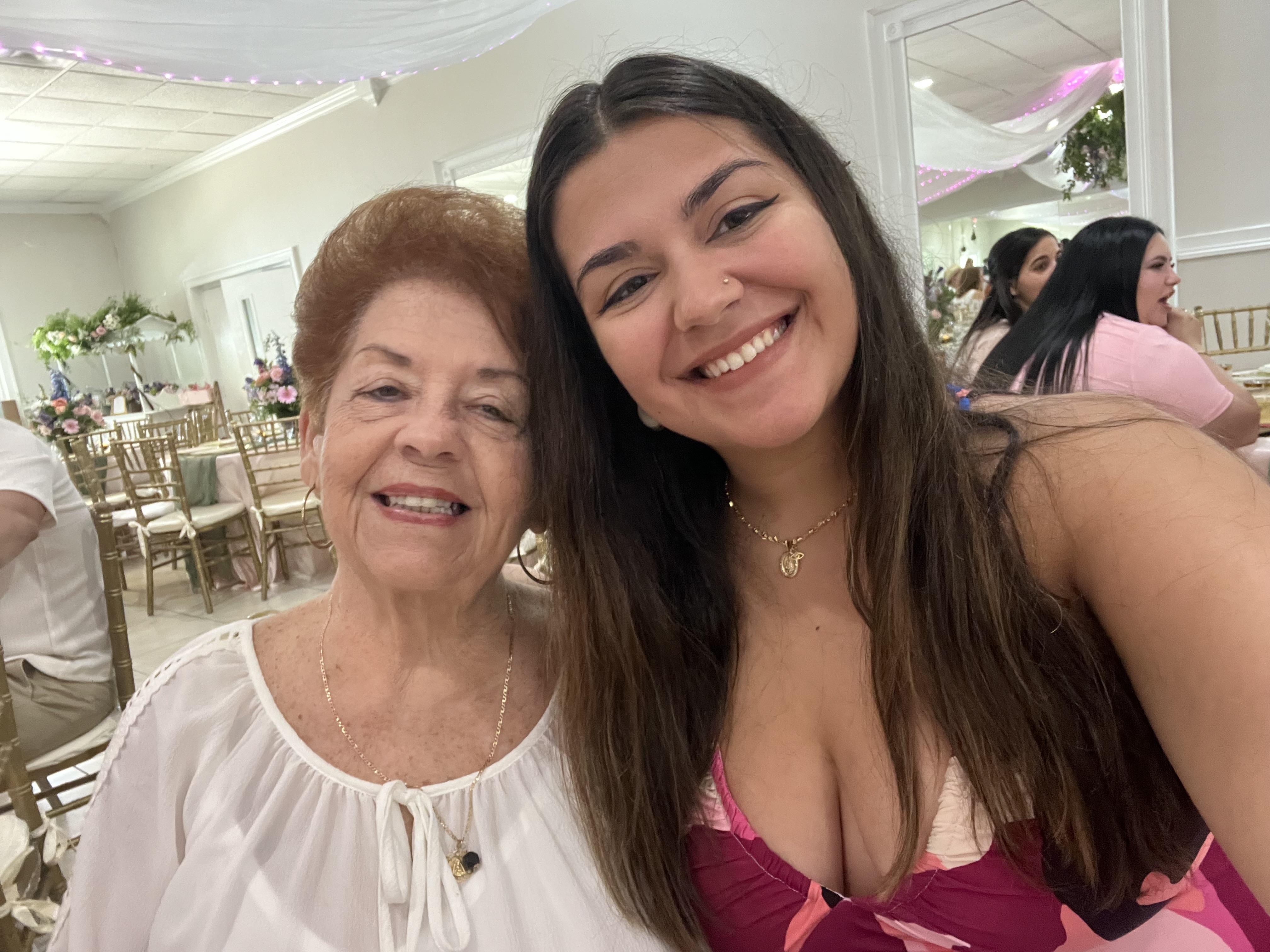 Two smiling women pose happily at a family event, celebrating together in a lively atmosphere.