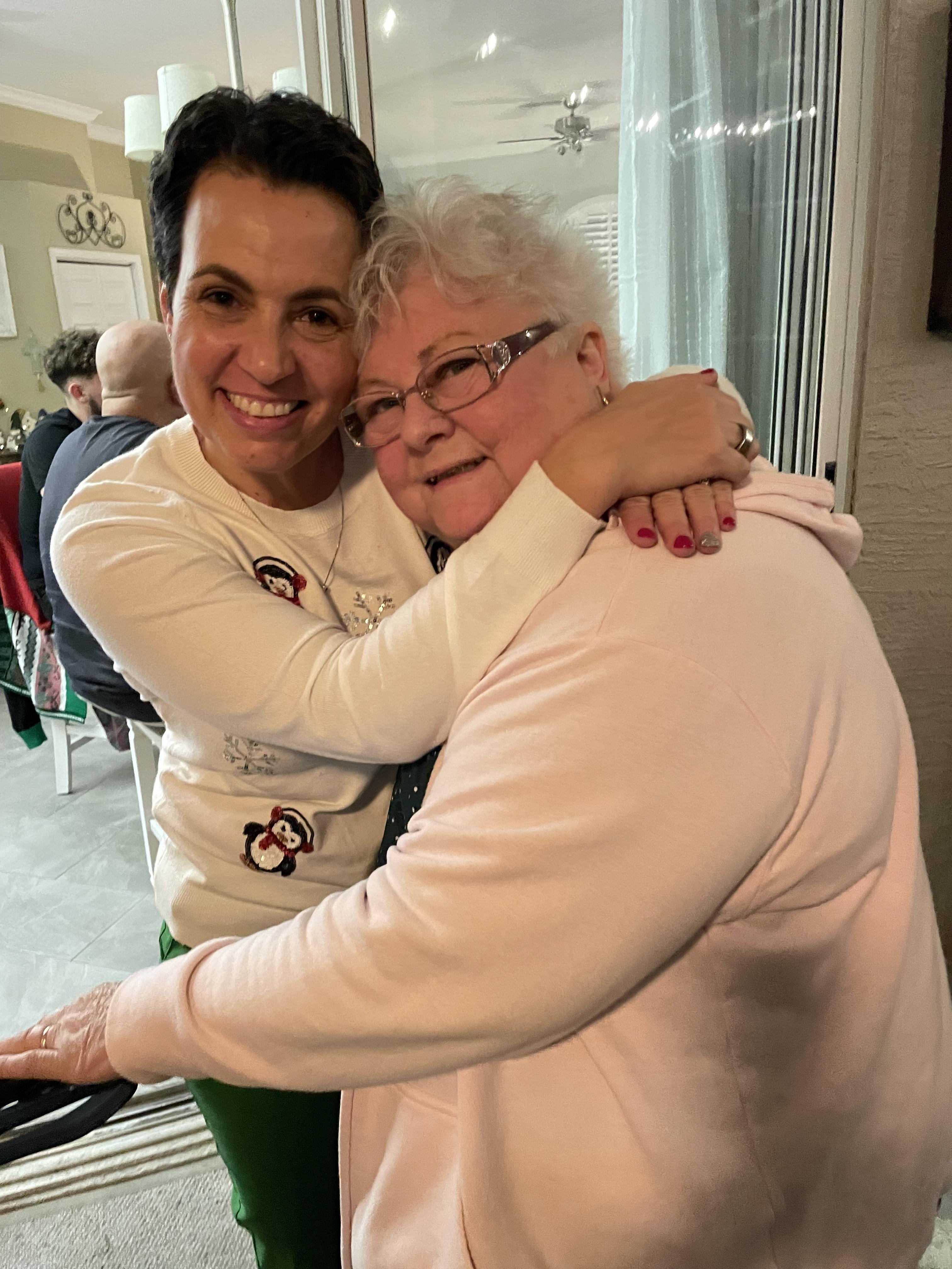 Two women joyfully hug each other while celebrating together in a cozy indoor setting.