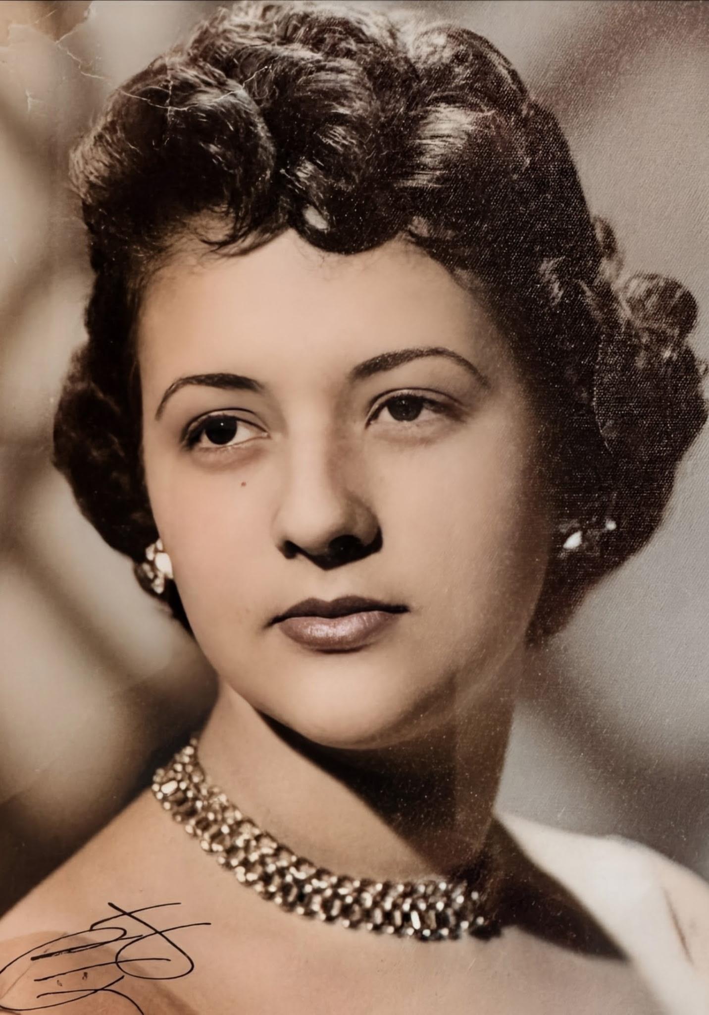 A confident woman poses with curly hair and elegant jewelry, capturing vintage fashion charm.