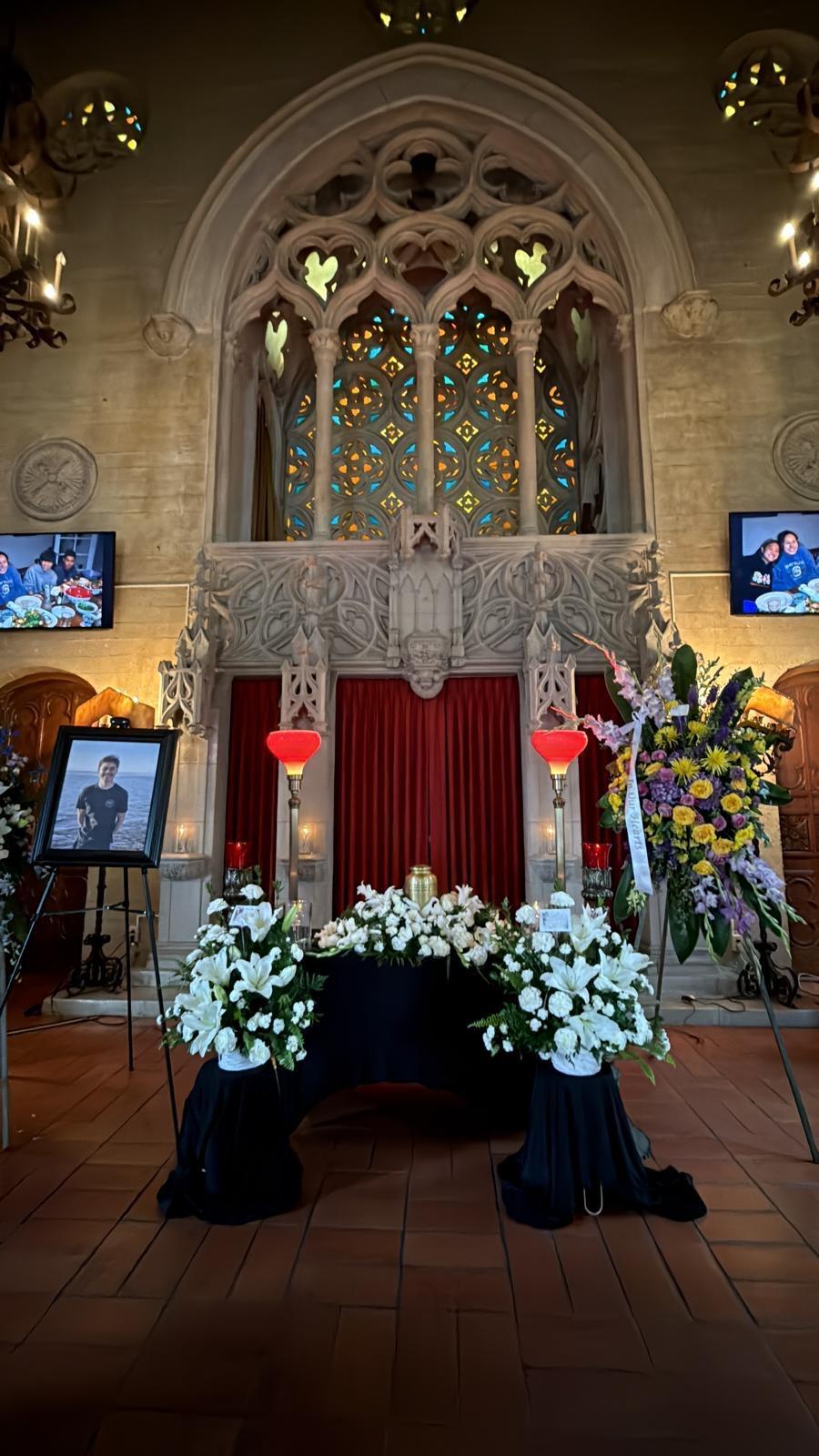 A tribute setup featuring flowers, photographs, and lighting in an ornate venue.