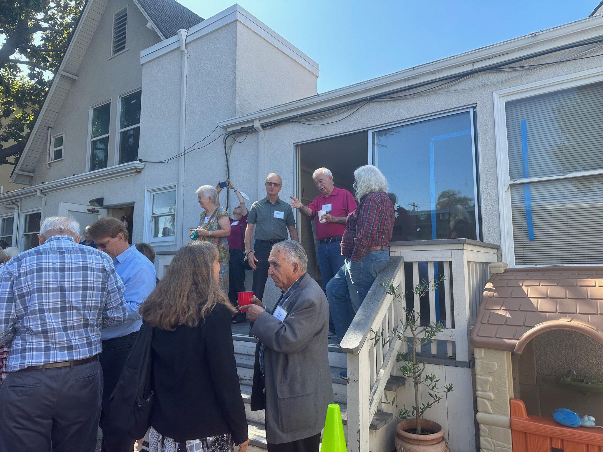 Community members socialize outdoors on a sunny day, sharing conversations and laughter.