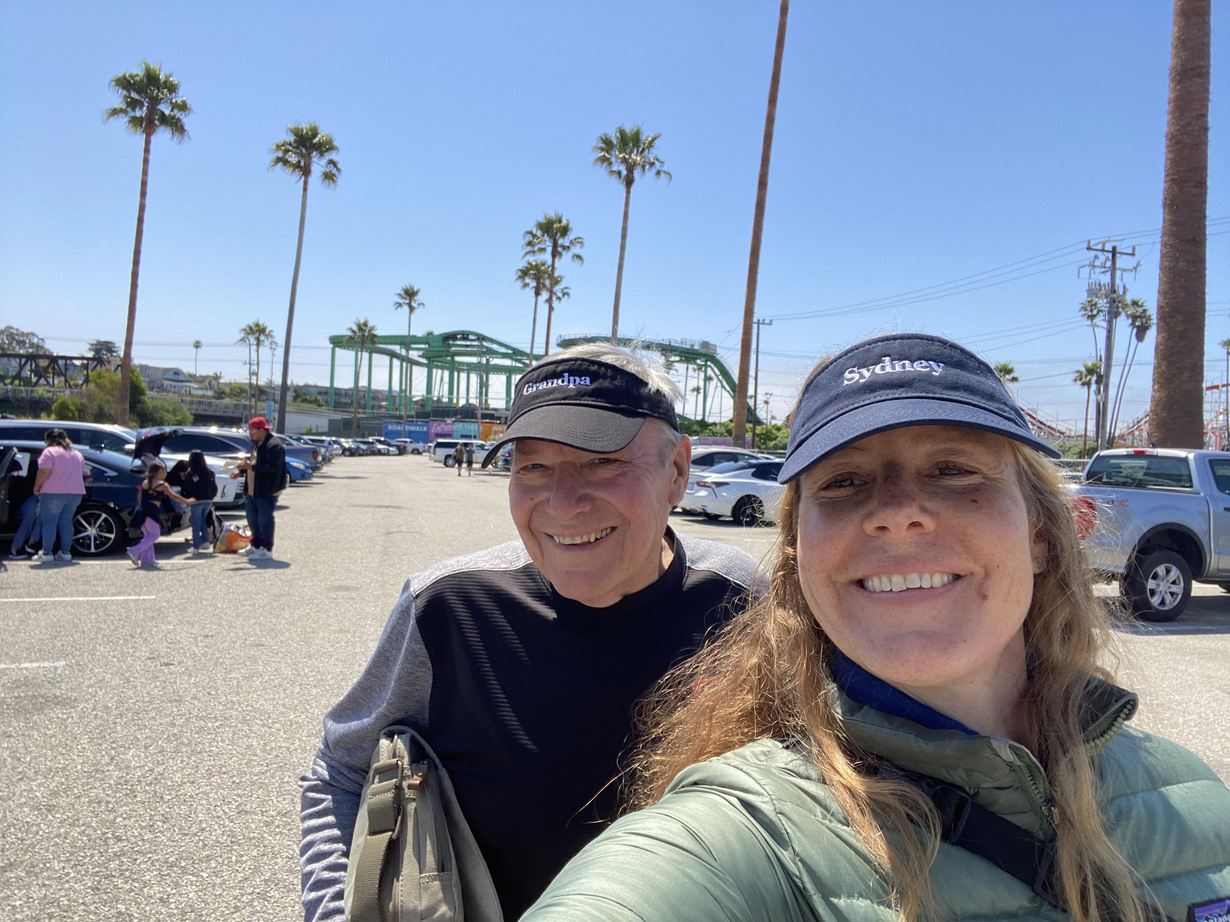 Two people smile and pose for a selfie in a vibrant outdoor setting with palm trees.