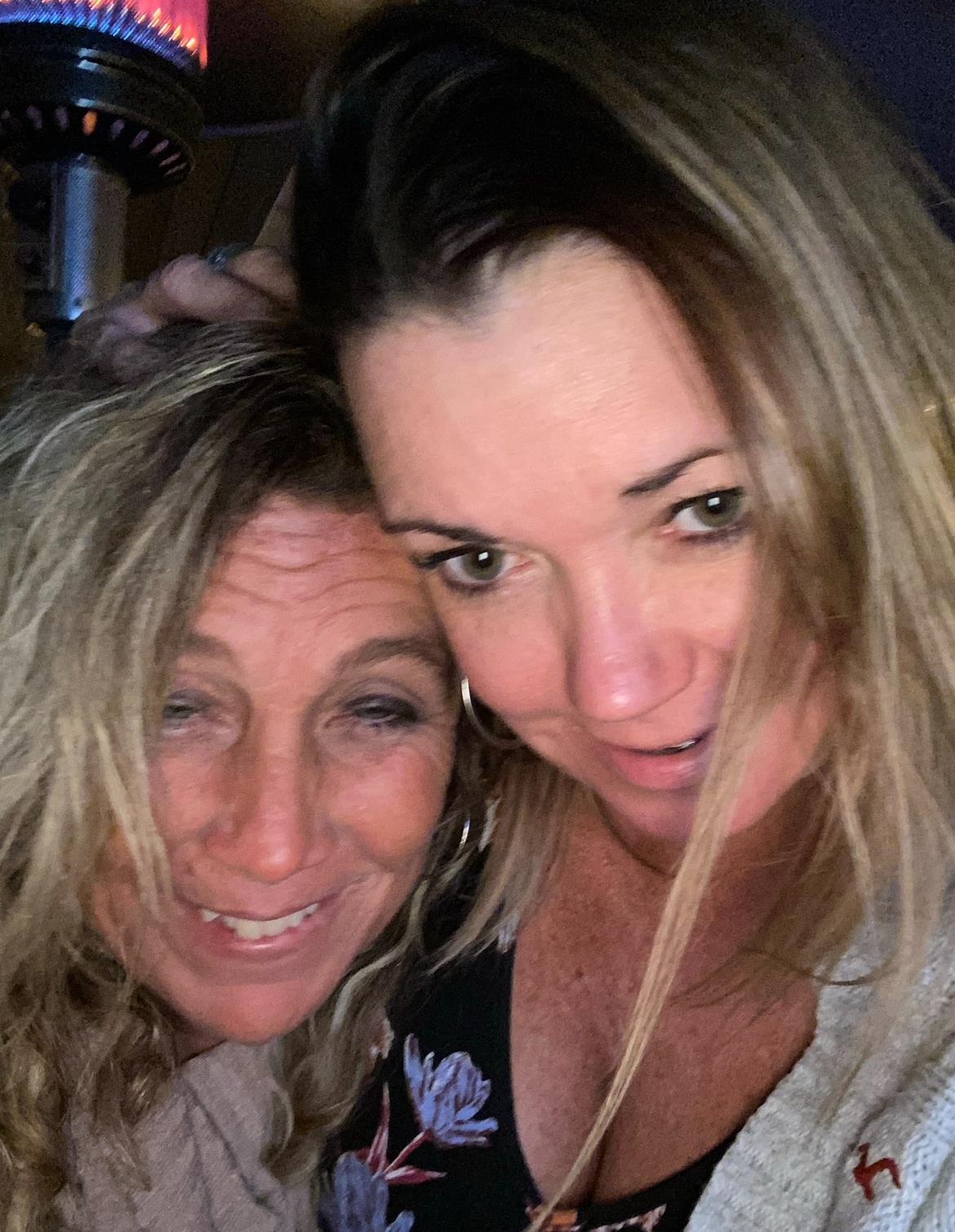 Two women share a joyful moment while posing closely together under a patio heater.