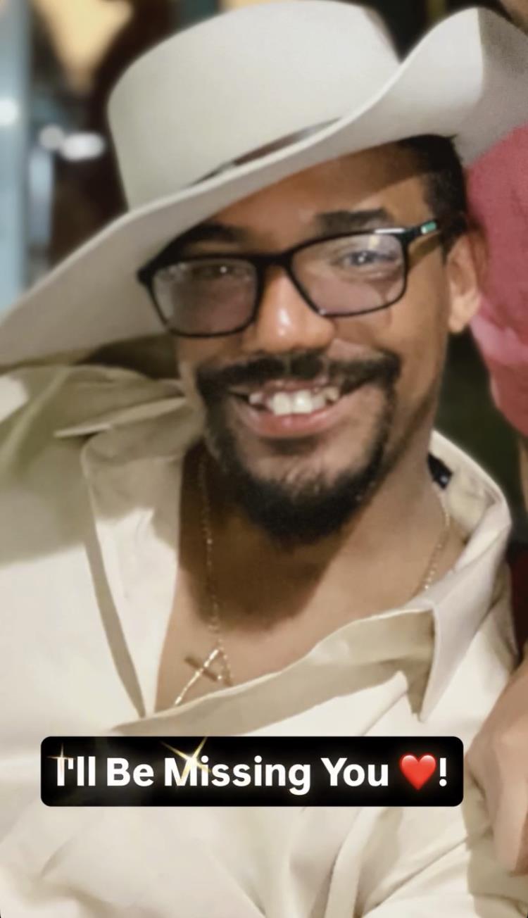 Man with a big smile wears stylish glasses and a hat, enjoying a fun moment at a social gathering.