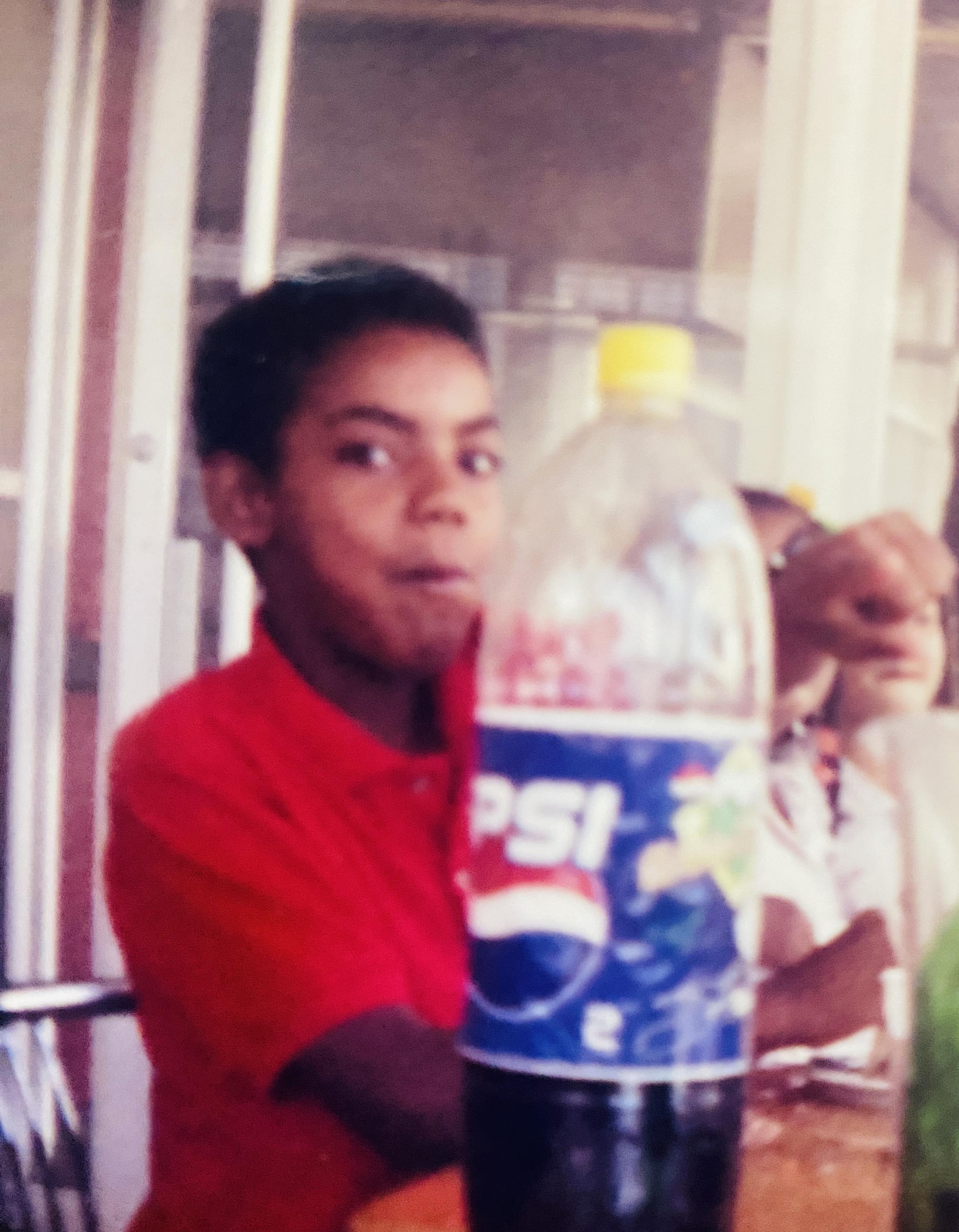Young boy holds a drink and smiles while enjoying a fun moment with friends outdoors.