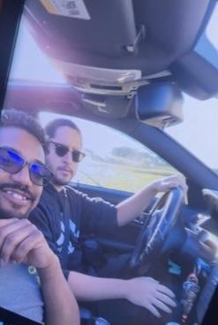 Two friends smile while driving in a sleek car on a bright sunny day.