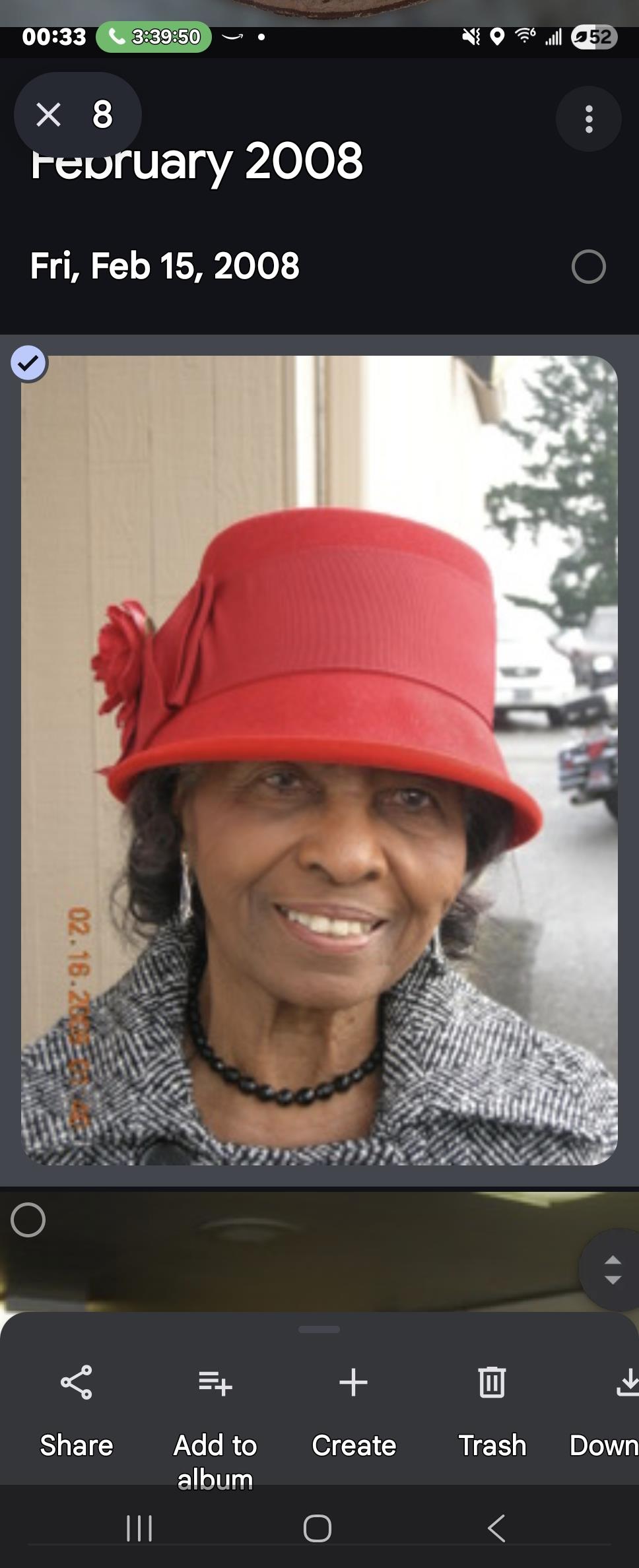 An elderly woman wearing a red hat and necklace smiles brightly outdoors near a busy street.