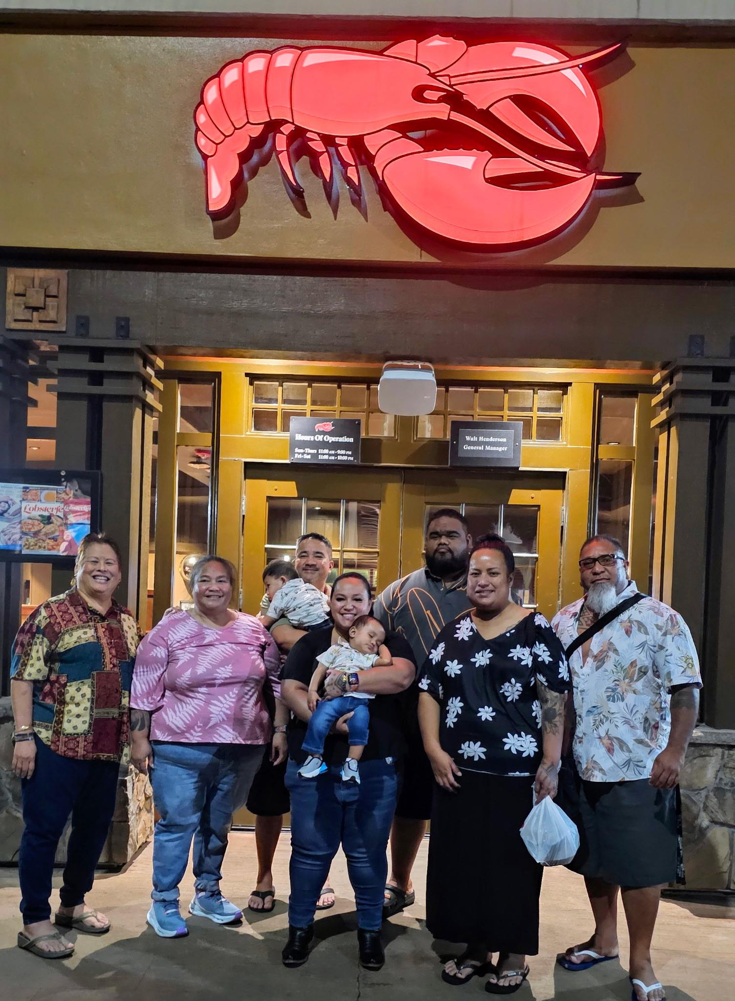 Group of family members smiles for a picture outside a seafood restaurant with bright signage.