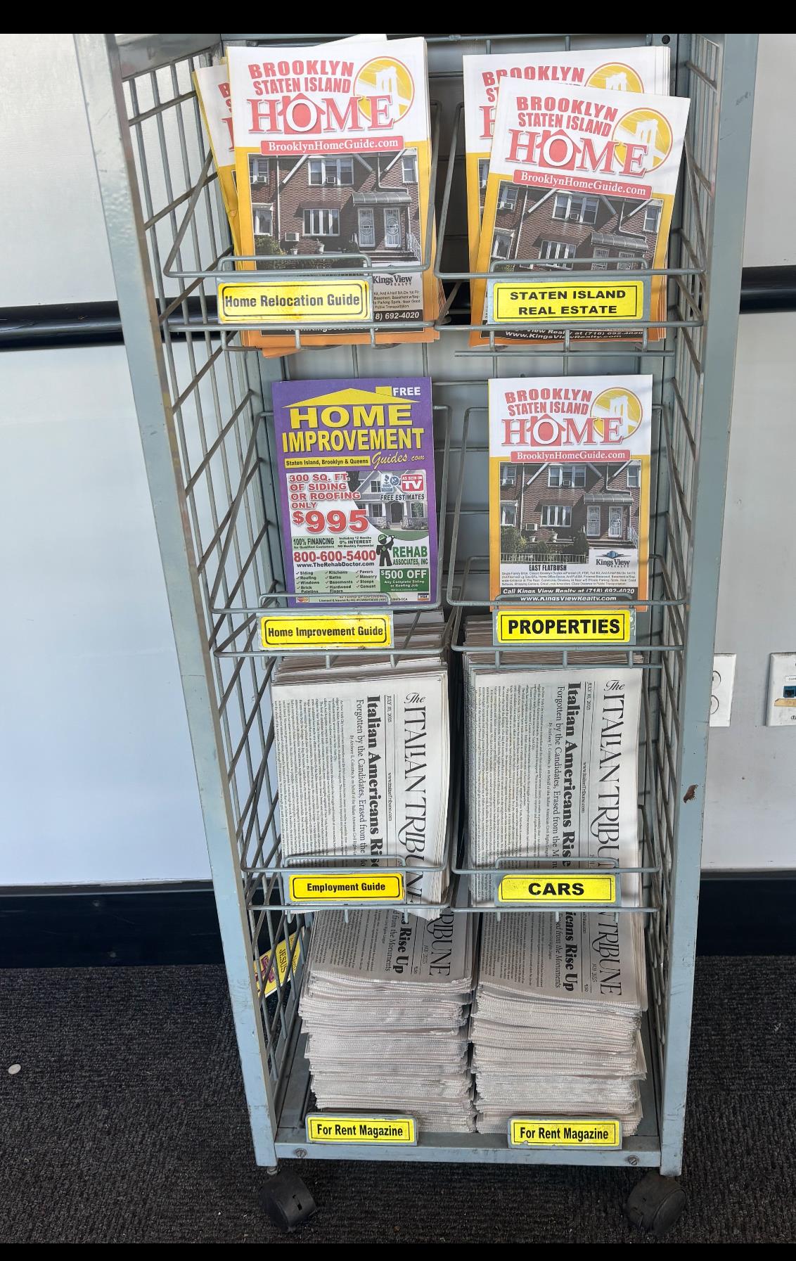 A metal display rack holds local guides and magazines on Staten Island, organized by category.