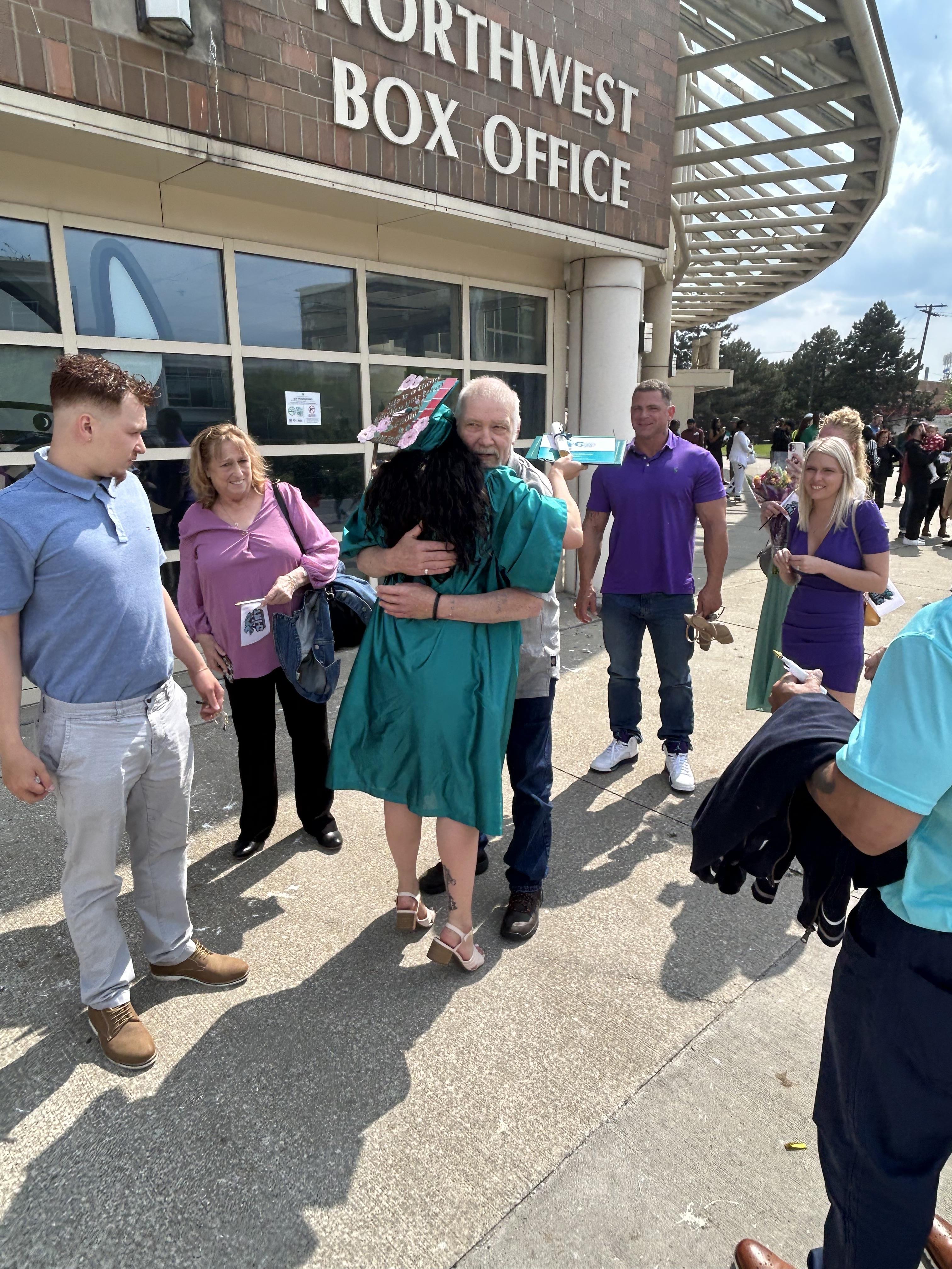 A group celebrates graduation outside the Northwest Box Office, sharing hugs and smiles.