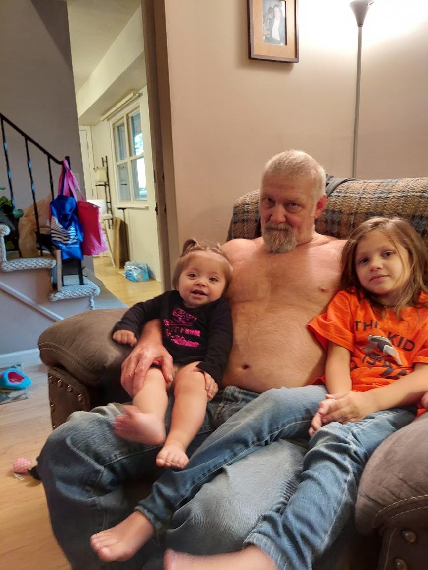 A grandfather sits on a couch with his two grandchildren, sharing a joyful moment together.