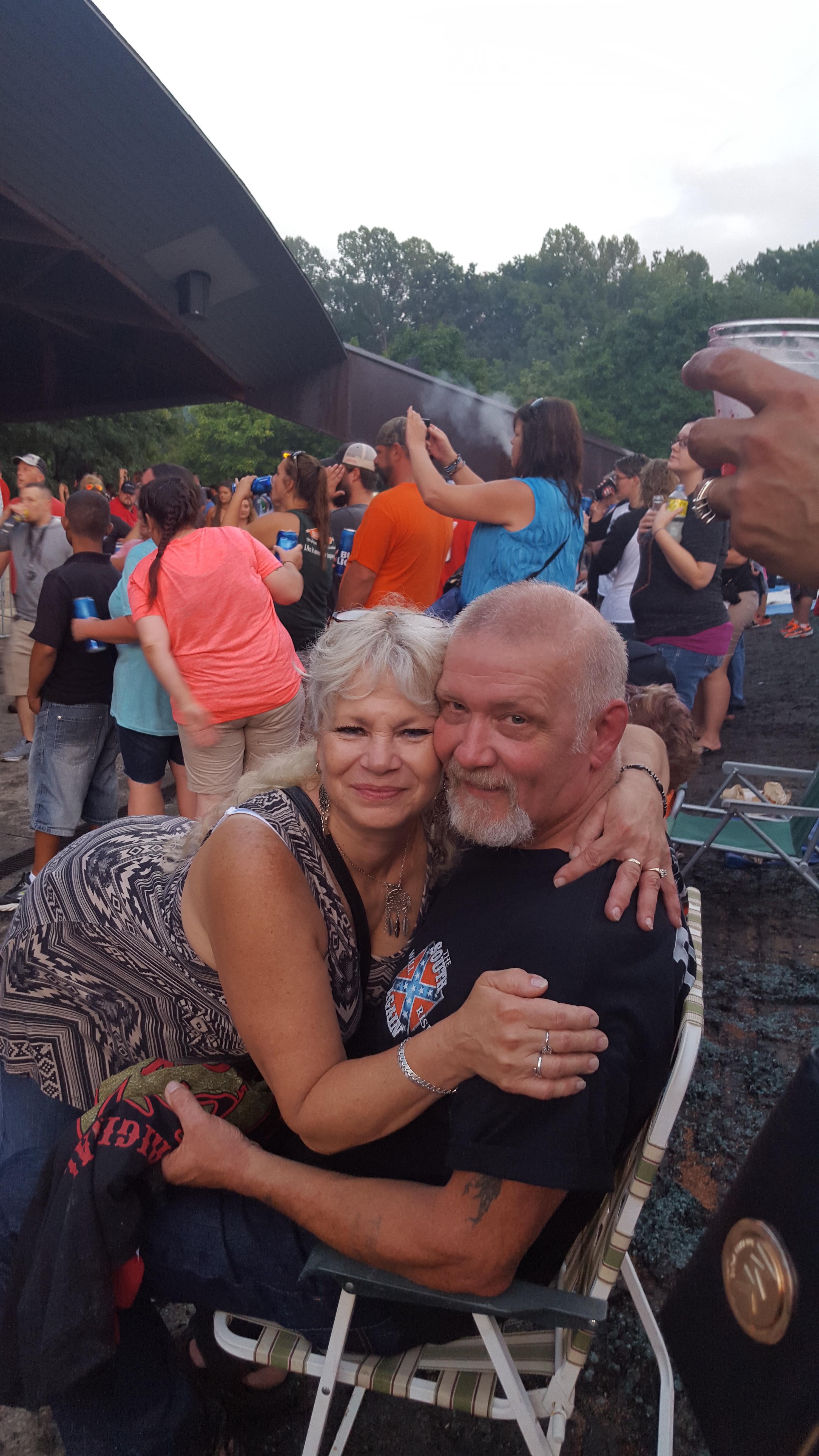 A happy couple embraces each other amidst a vibrant crowd at an outdoor event.
