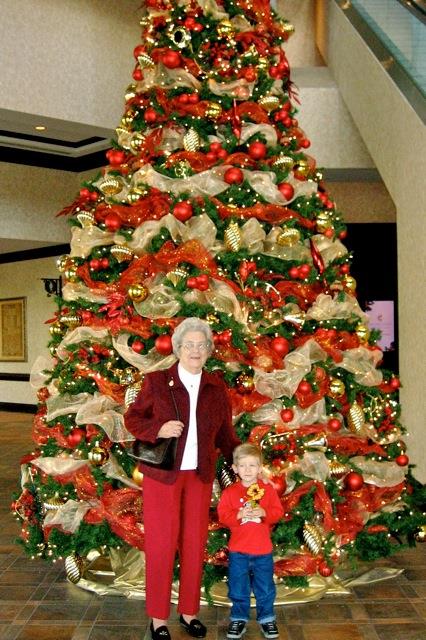 Grandmother and grandson smile together near a beautifully decorated Christmas tree.
