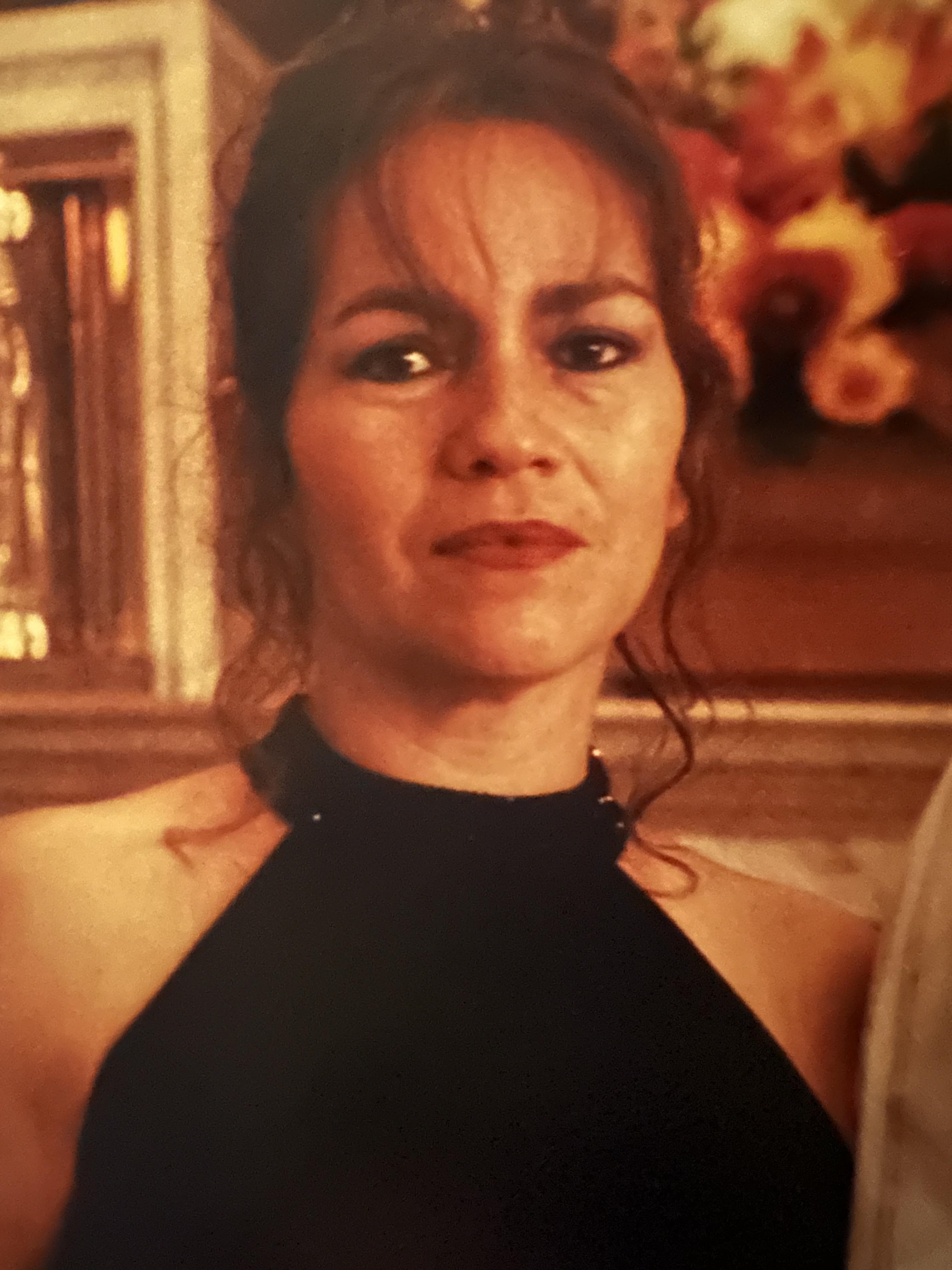 A woman stands confidently in a black dress at a festive event, exuding charm and elegance.