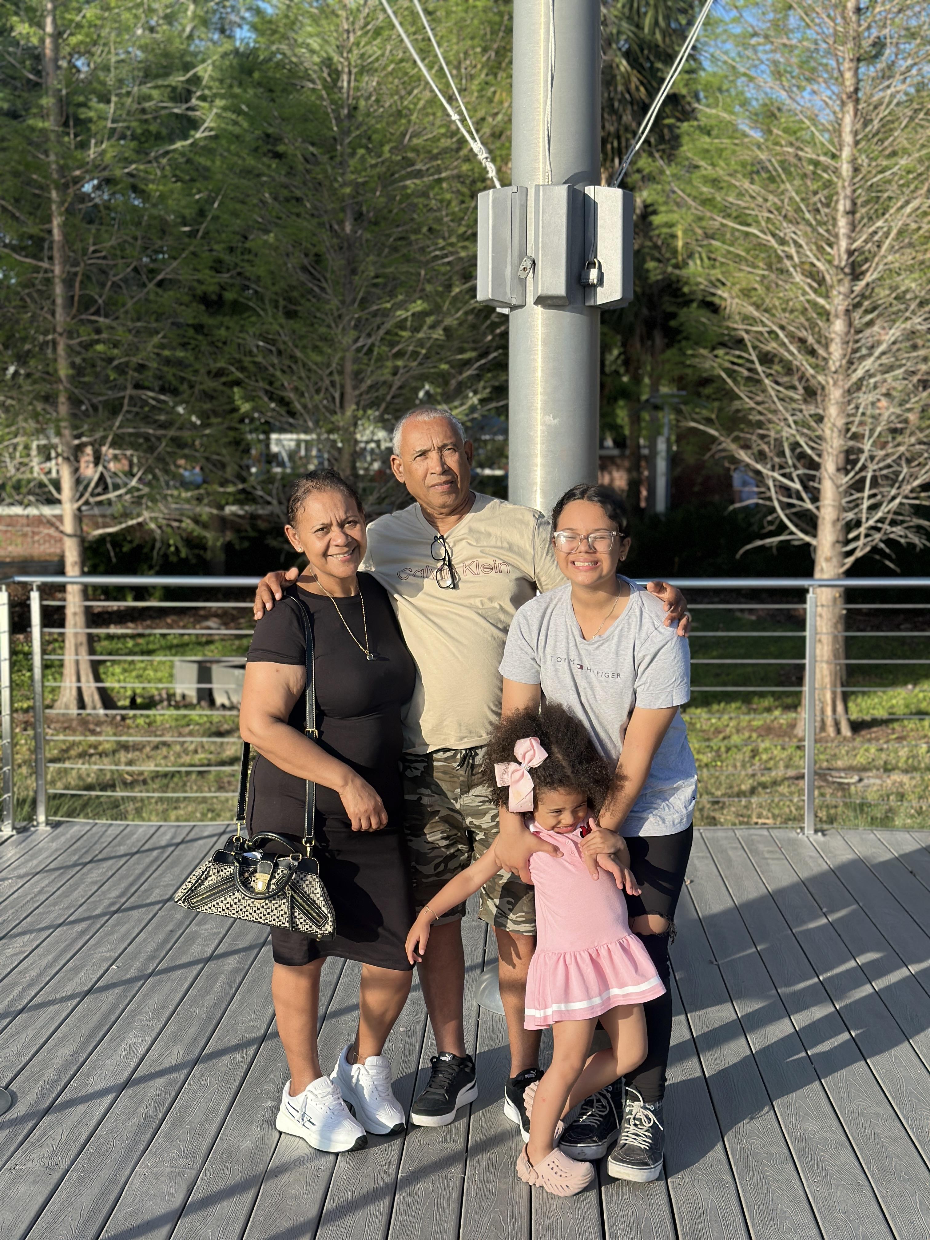 Four family members gather and pose for a cheerful photo on a sunny day in the park.