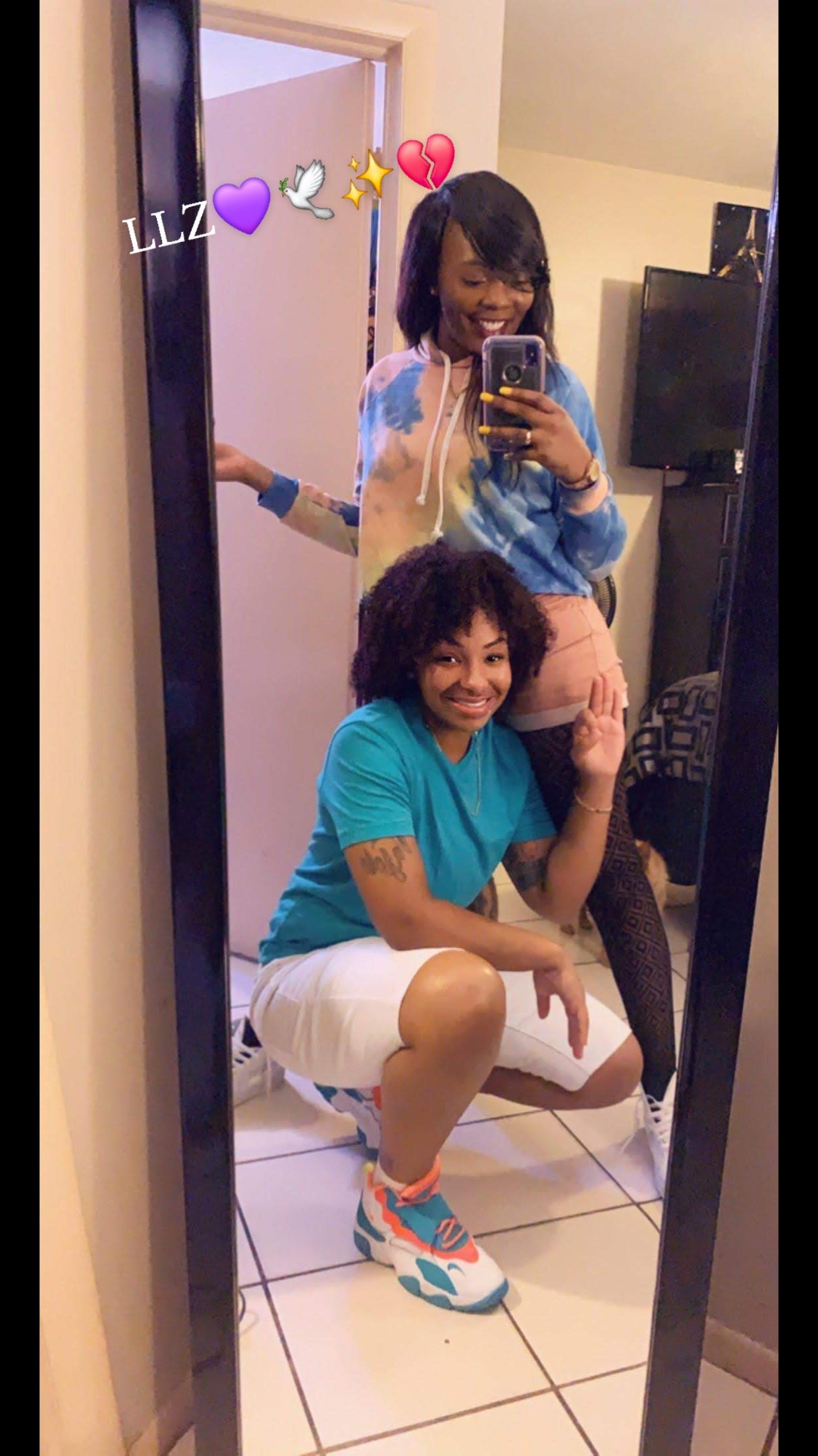 Two friends are enjoying a fun moment together, taking a playful selfie by a large mirror.
