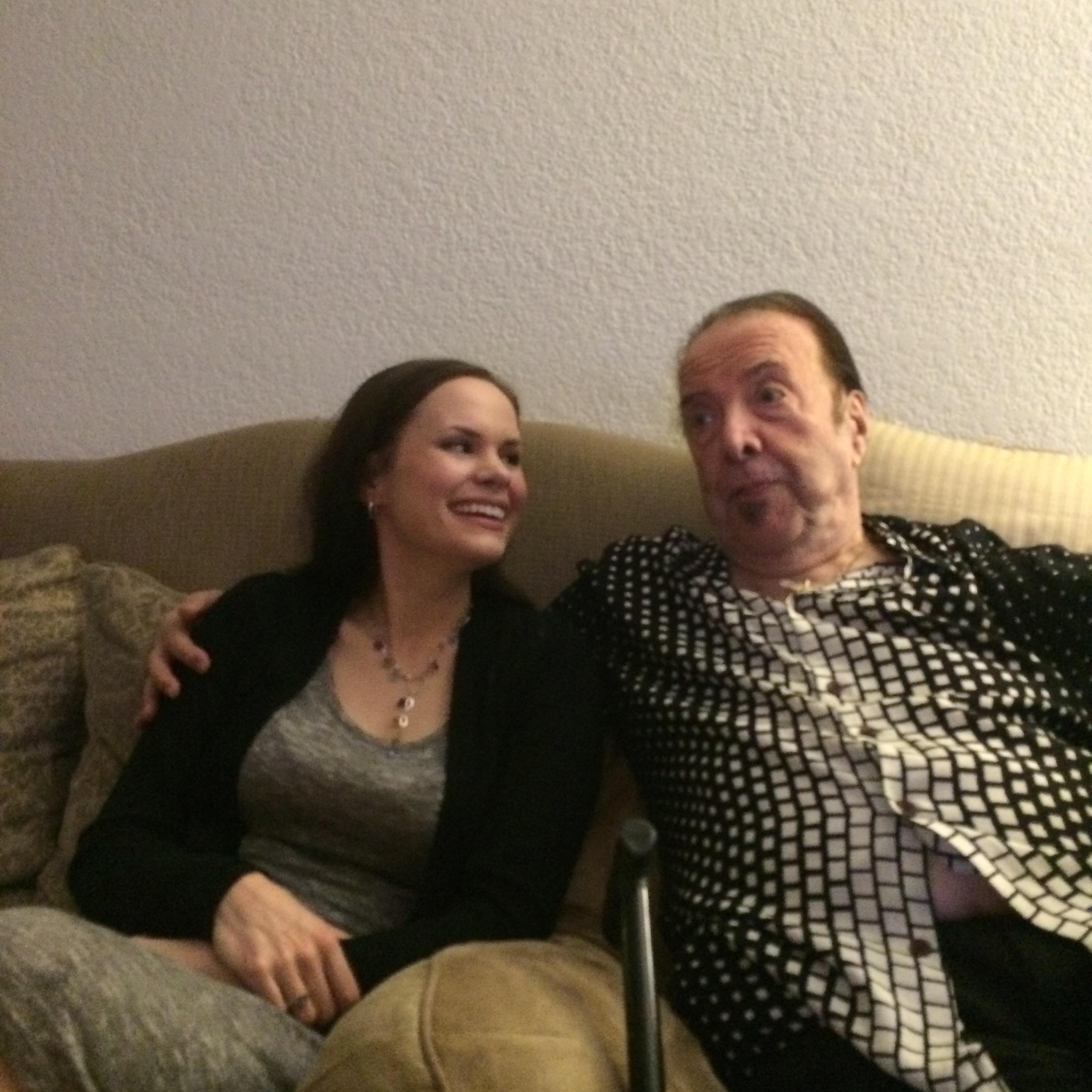 A man and a woman sit close together on a sofa, smiling and enjoying each other's company.