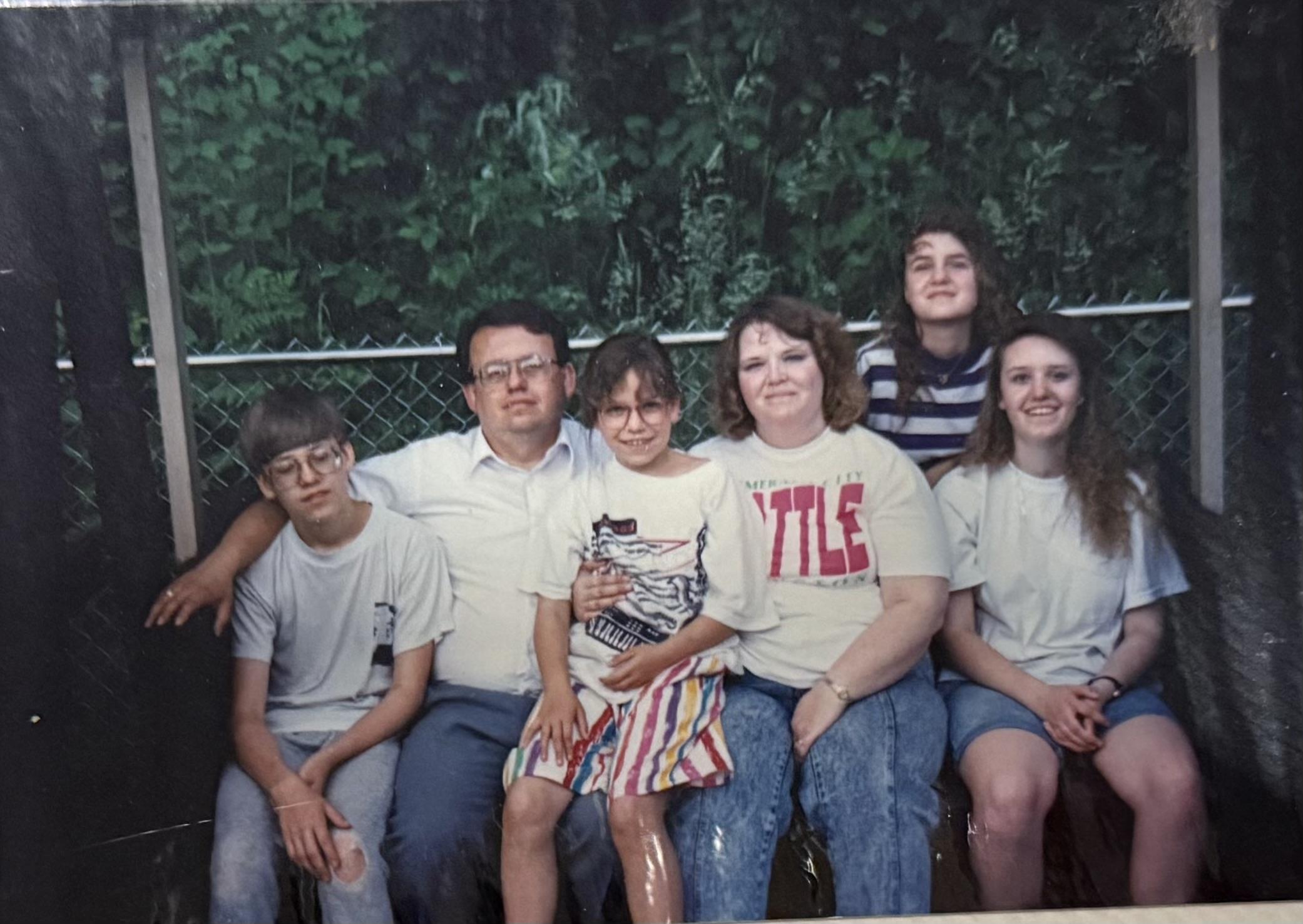 Family members pose together outdoors in summer attire, smiling and sharing a special moment.